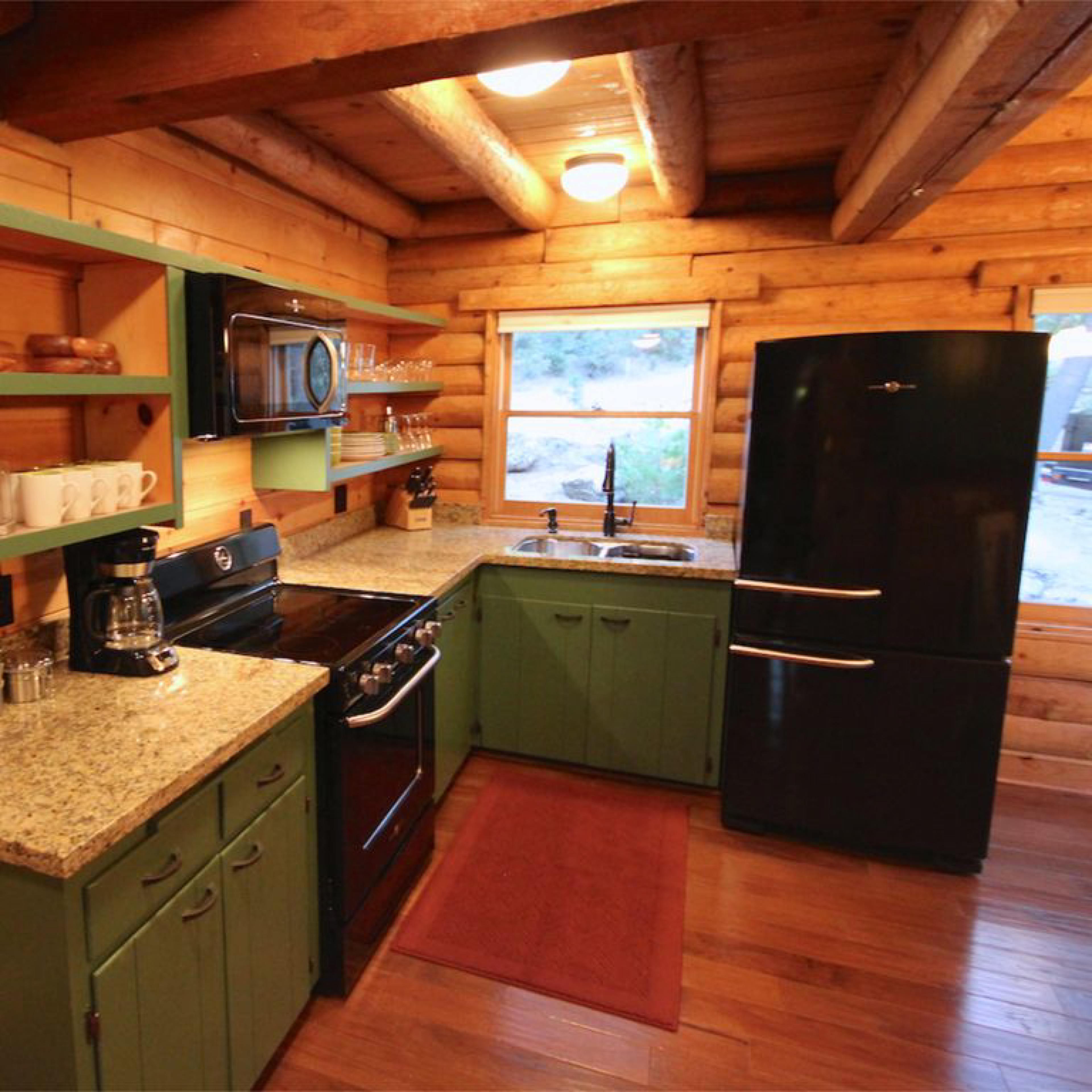 The kitchen features wooden walls and beams, with green cabinetry, a black refrigerator, and granite countertops.