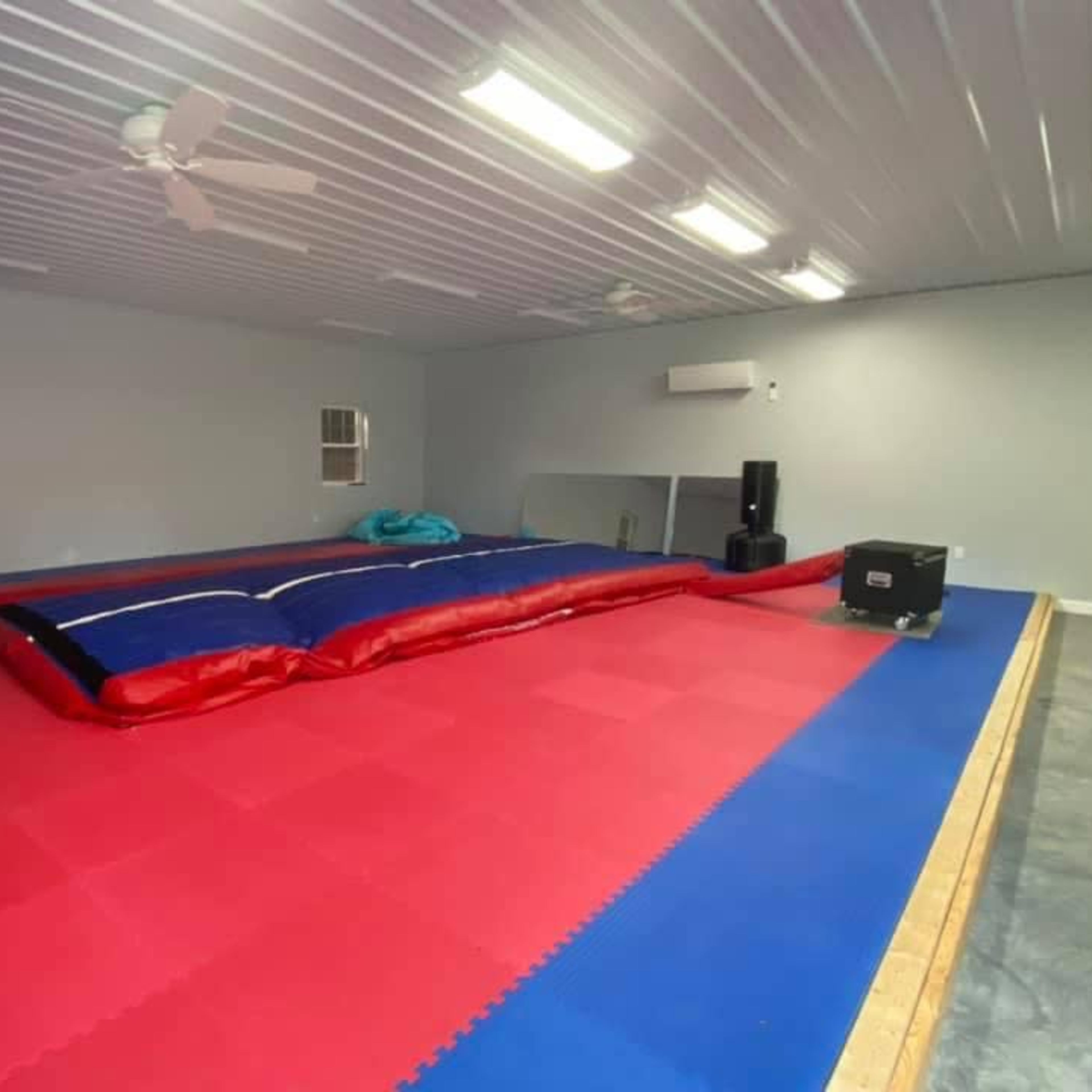 A large indoor gymnasium with a red and blue gymnastics mat, a foam pit, and some equipment along the walls.