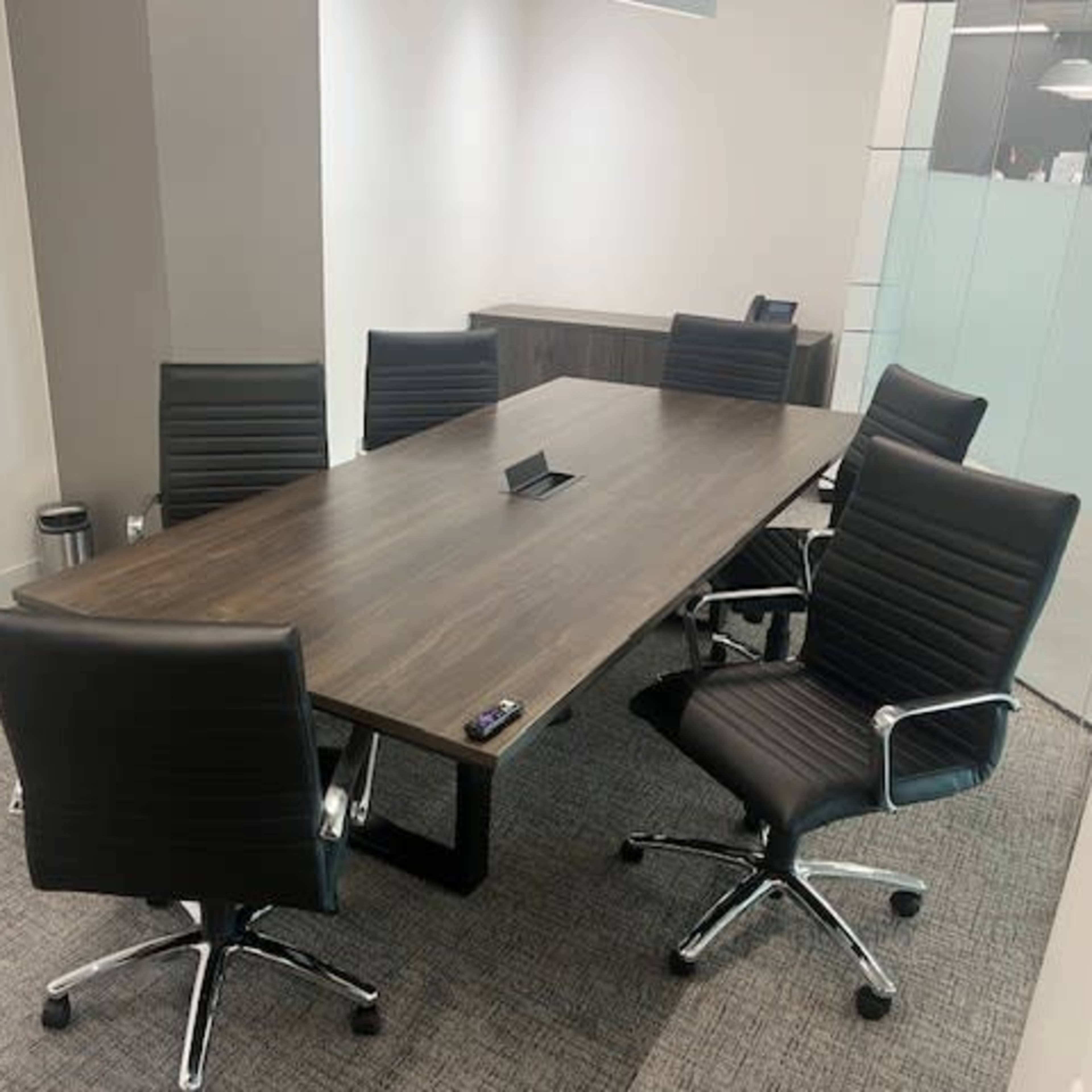 A modern conference room features a long table surrounded by six black office chairs.