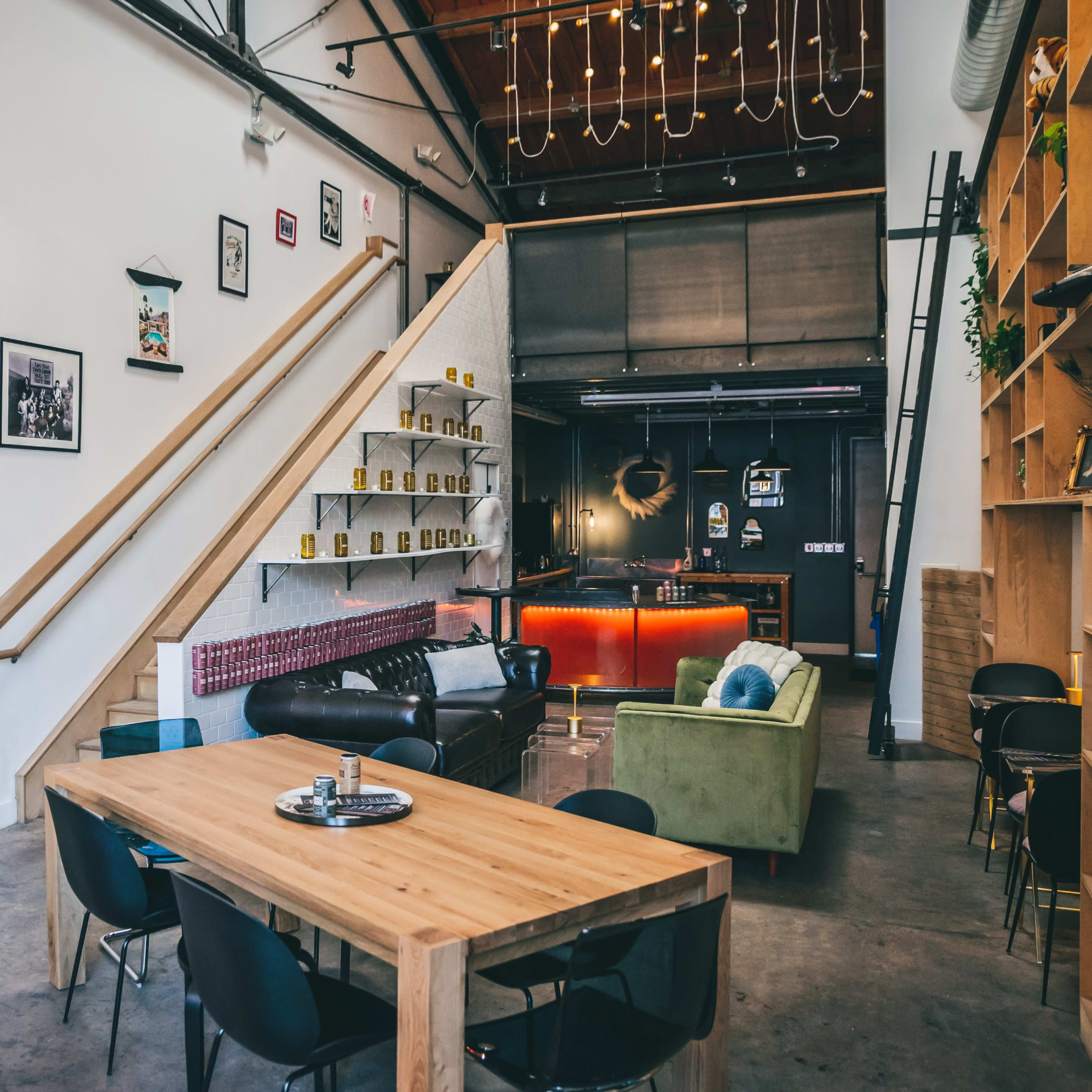A modern, open interior space featuring a dining table, various seating arrangements, and a staircase leading to an upper level, with decorative elements on the walls.