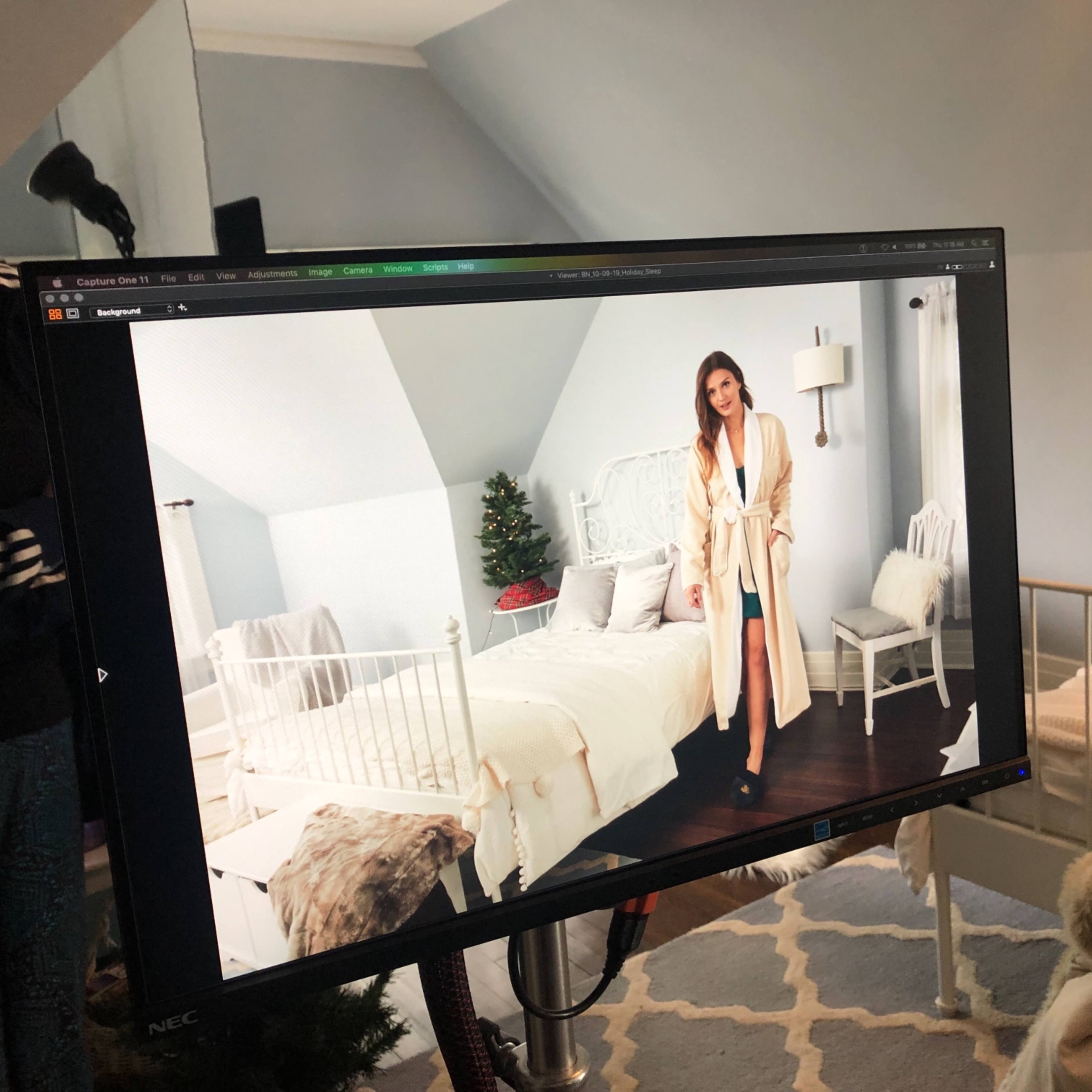 A bedroom scene is displayed on a monitor, featuring a woman in a robe standing next to a bed, with holiday decorations visible in the background.