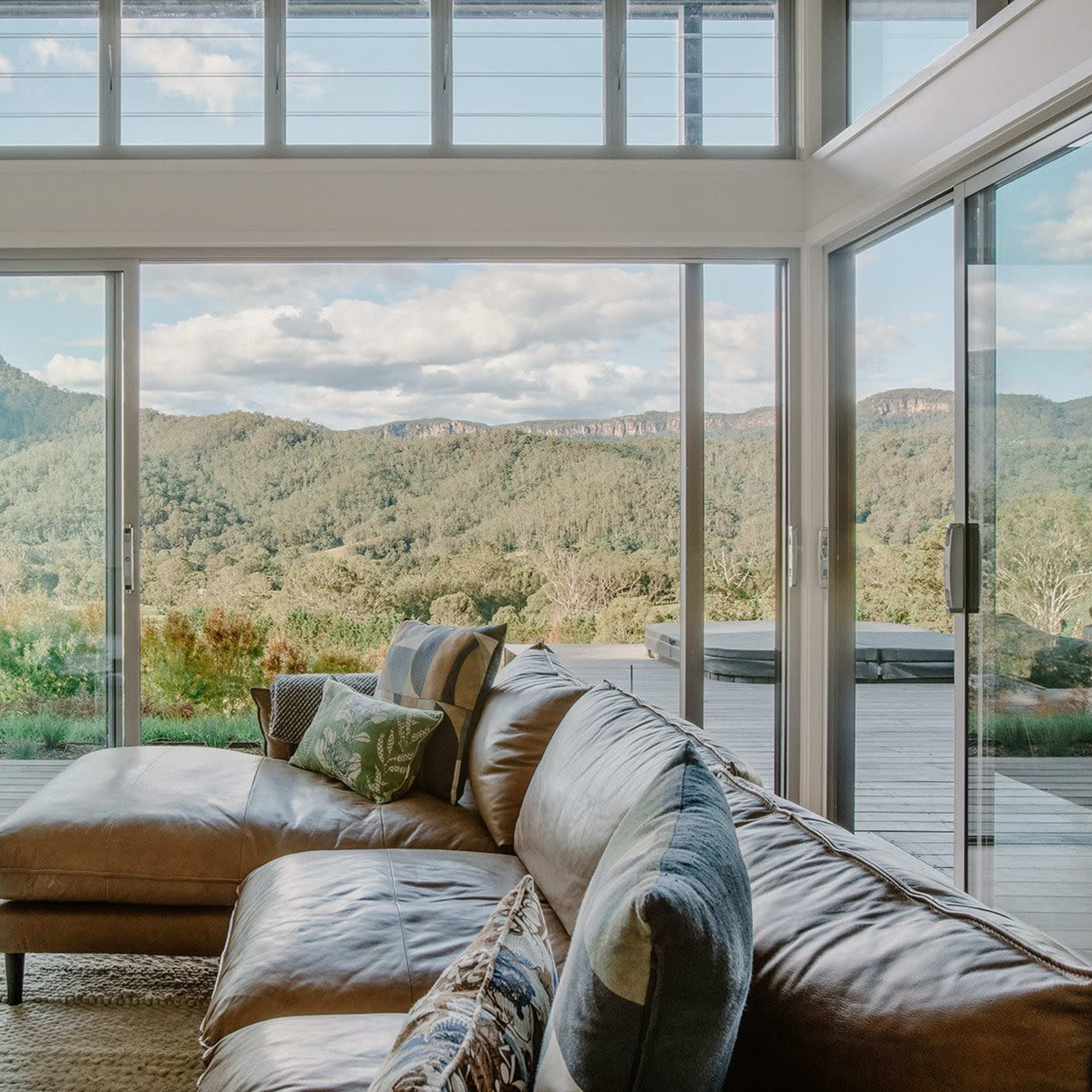 A modern living room features a large sectional sofa and expansive windows that provide a view of rolling hills and mountains in the distance.