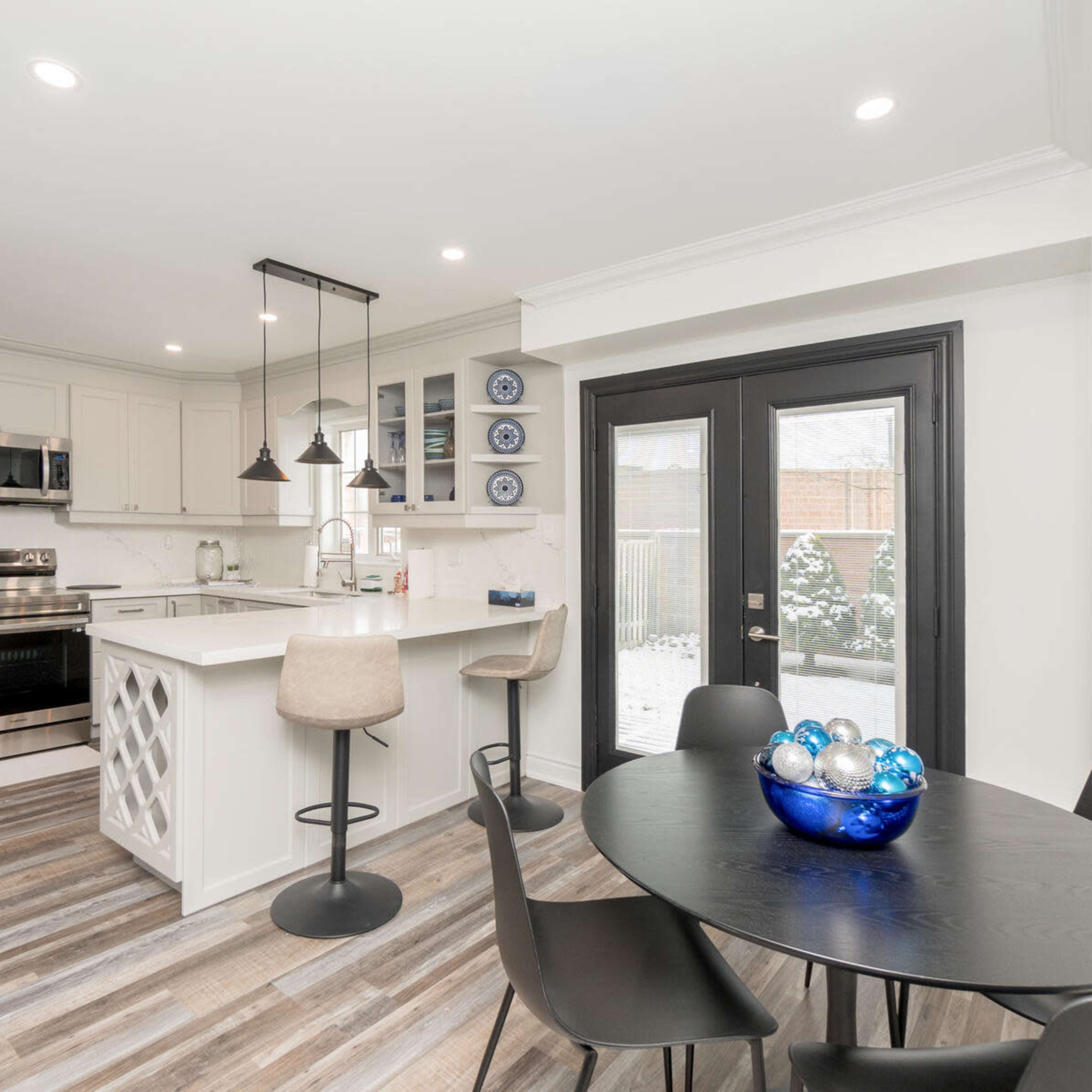 A modern kitchen with stainless steel appliances, a central island, and a dining area featuring a round table with a blue glass bowl.