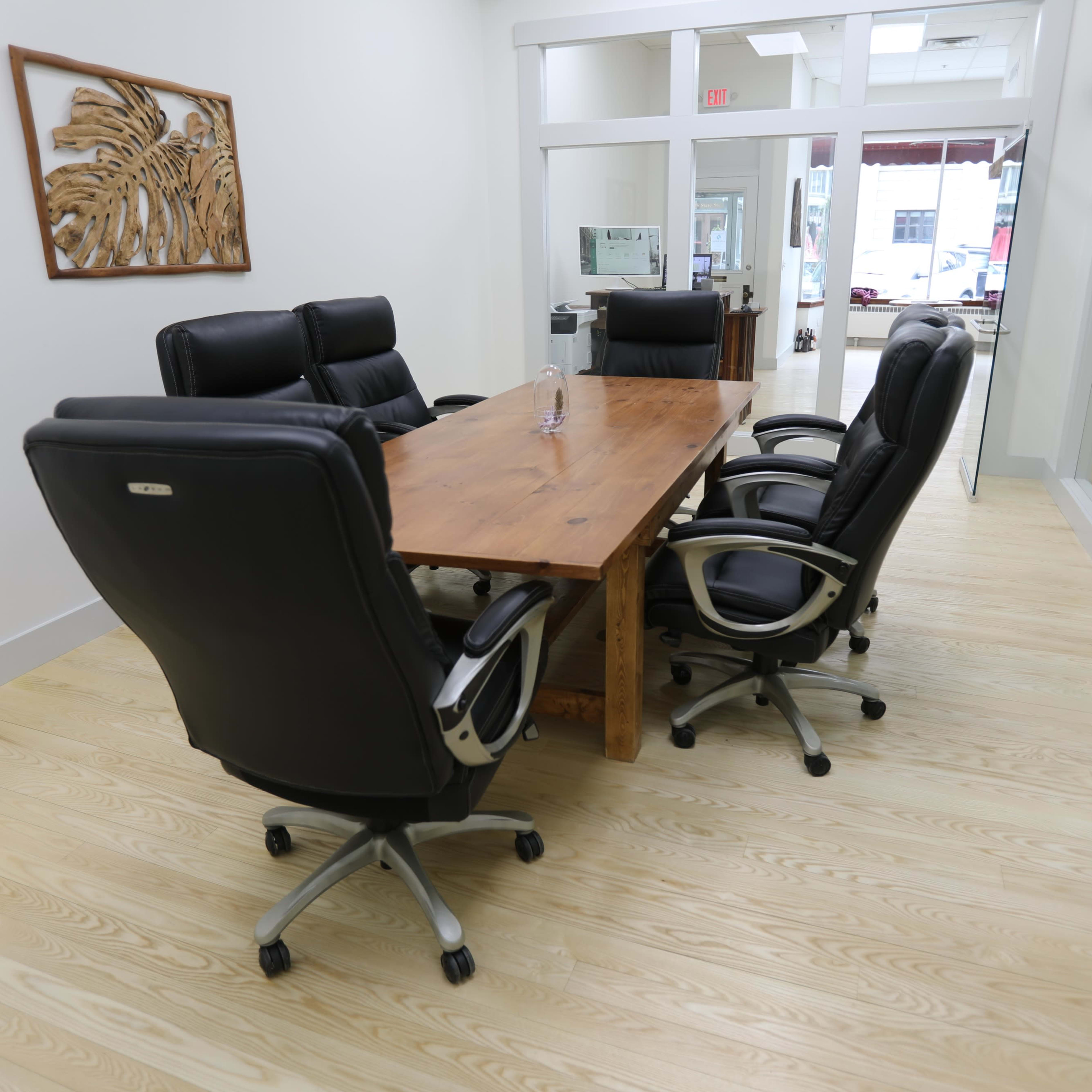 A modern conference room features a wooden table surrounded by four black office chairs.
