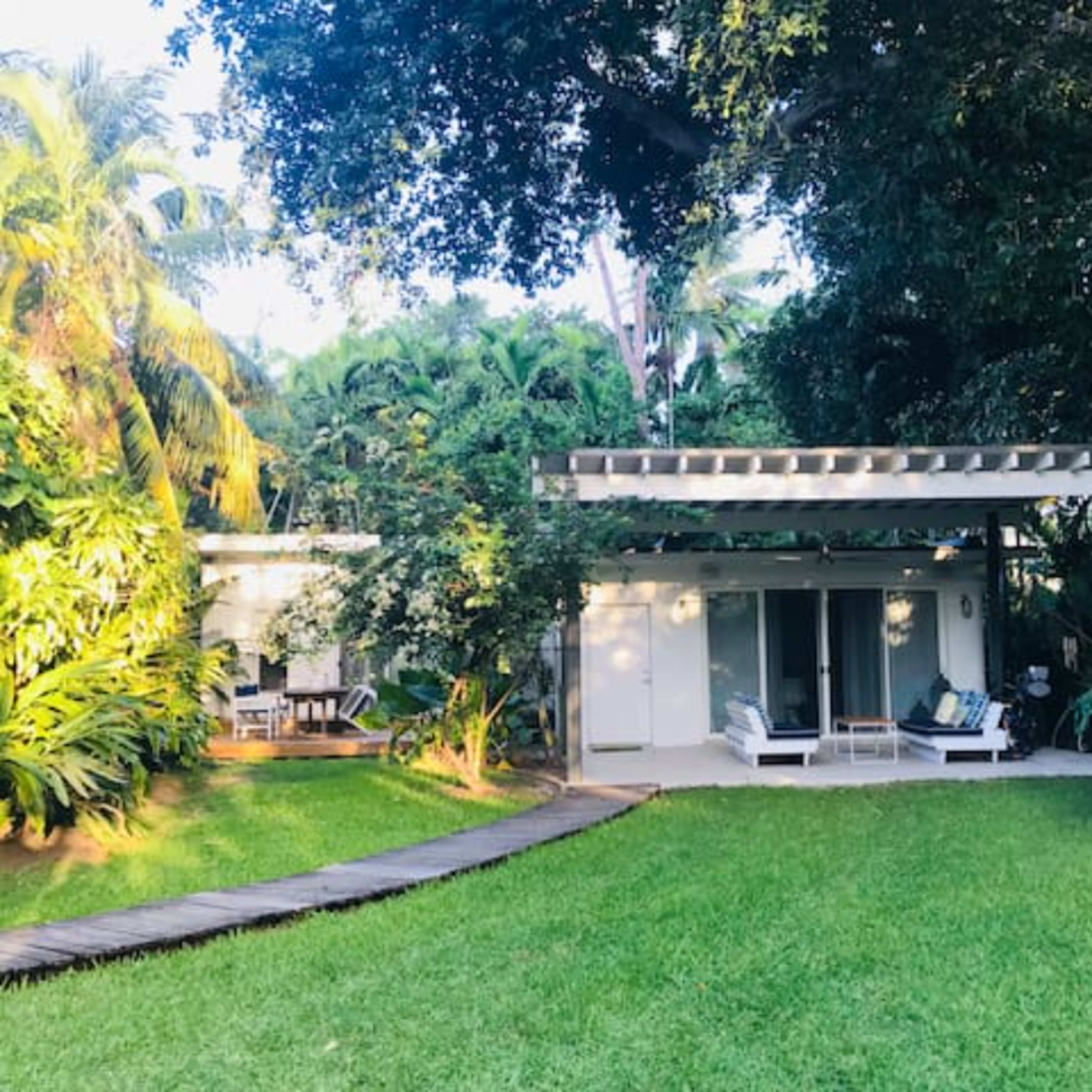 A modern home with a pergola sits surrounded by lush greenery and a manicured lawn.