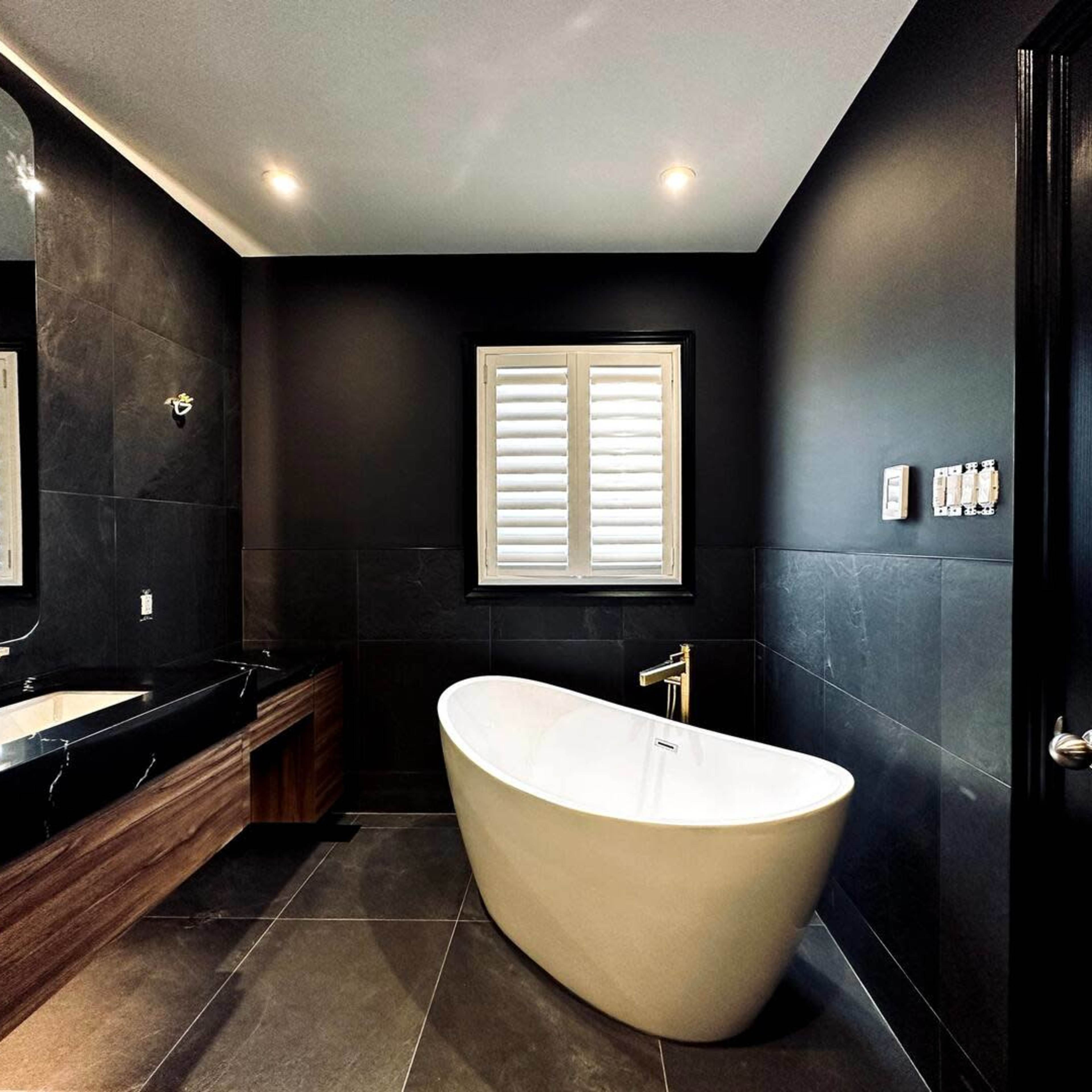 A modern bathroom featuring a freestanding white bathtub, dark walls, and a sleek wooden vanity.