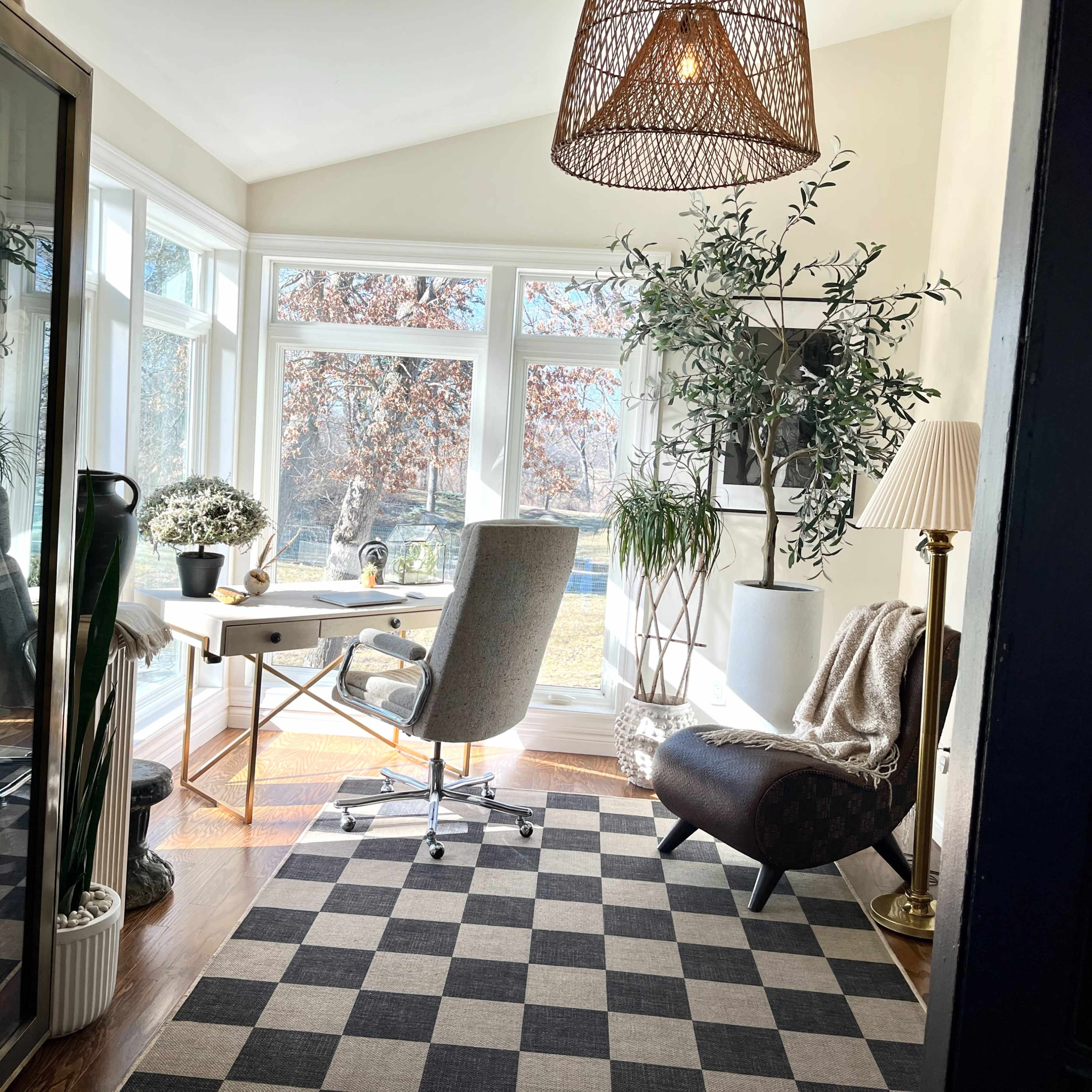 A sunlit home office with a desk, a chair, and plants arranged around large windows.