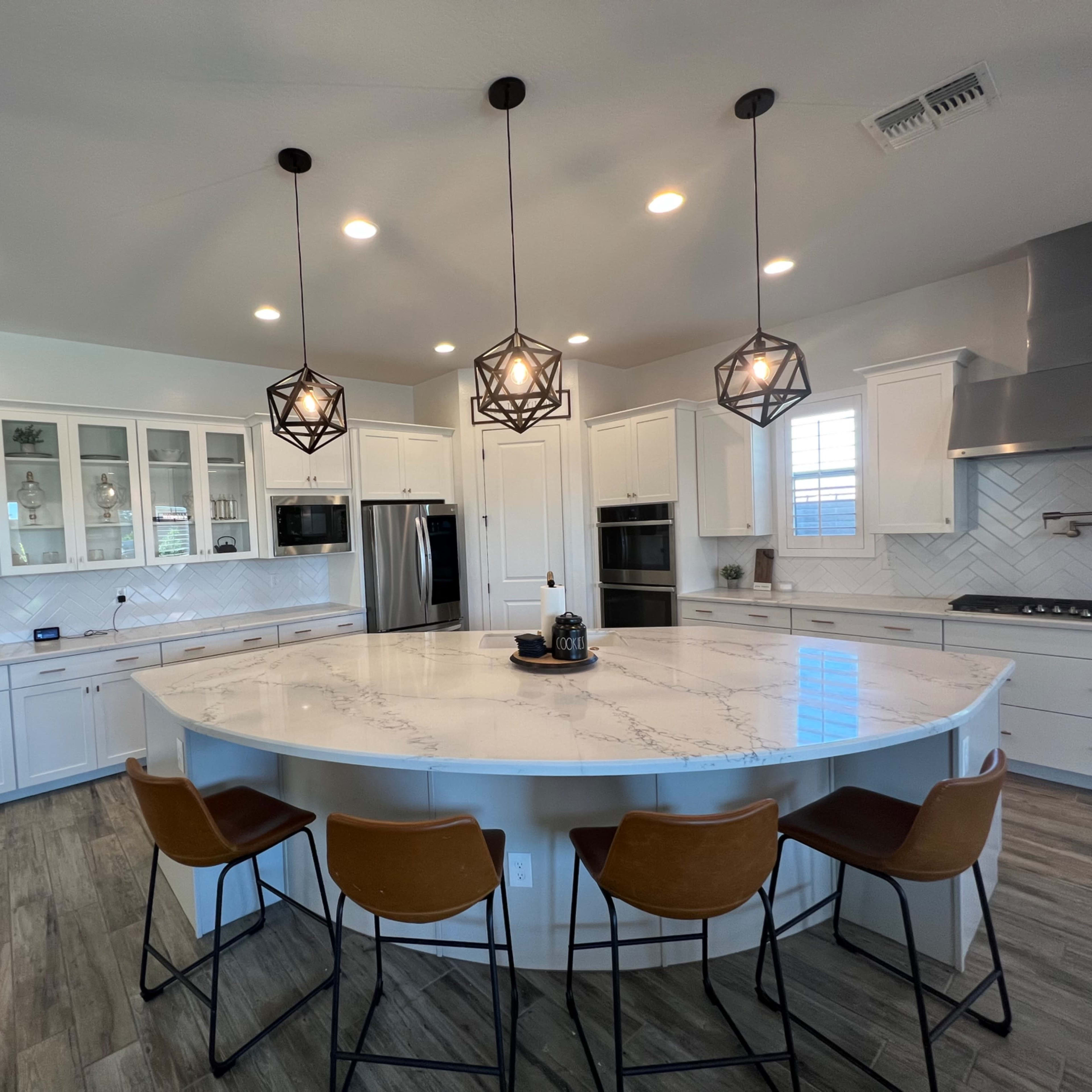 A modern kitchen featuring a large marble island with bar stools, white cabinetry, and pendant lighting.