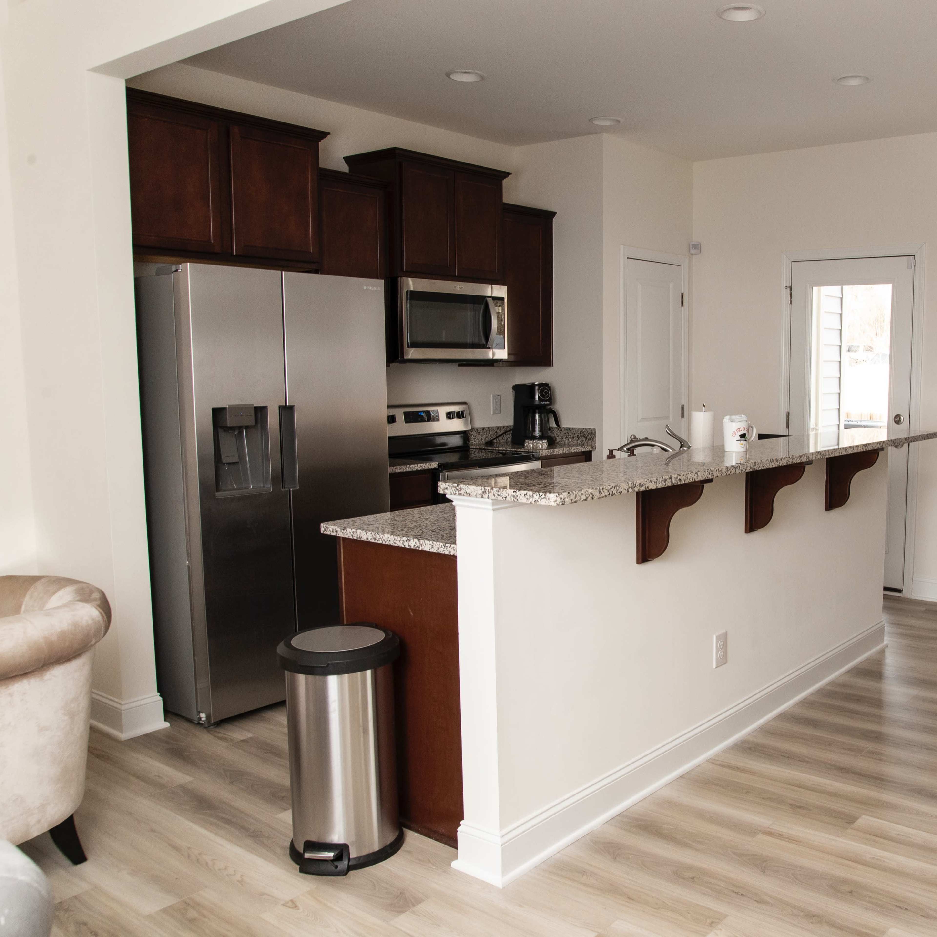 A modern open-concept kitchen features dark cabinetry, stainless steel appliances, and a granite countertop with a small dining area nearby.