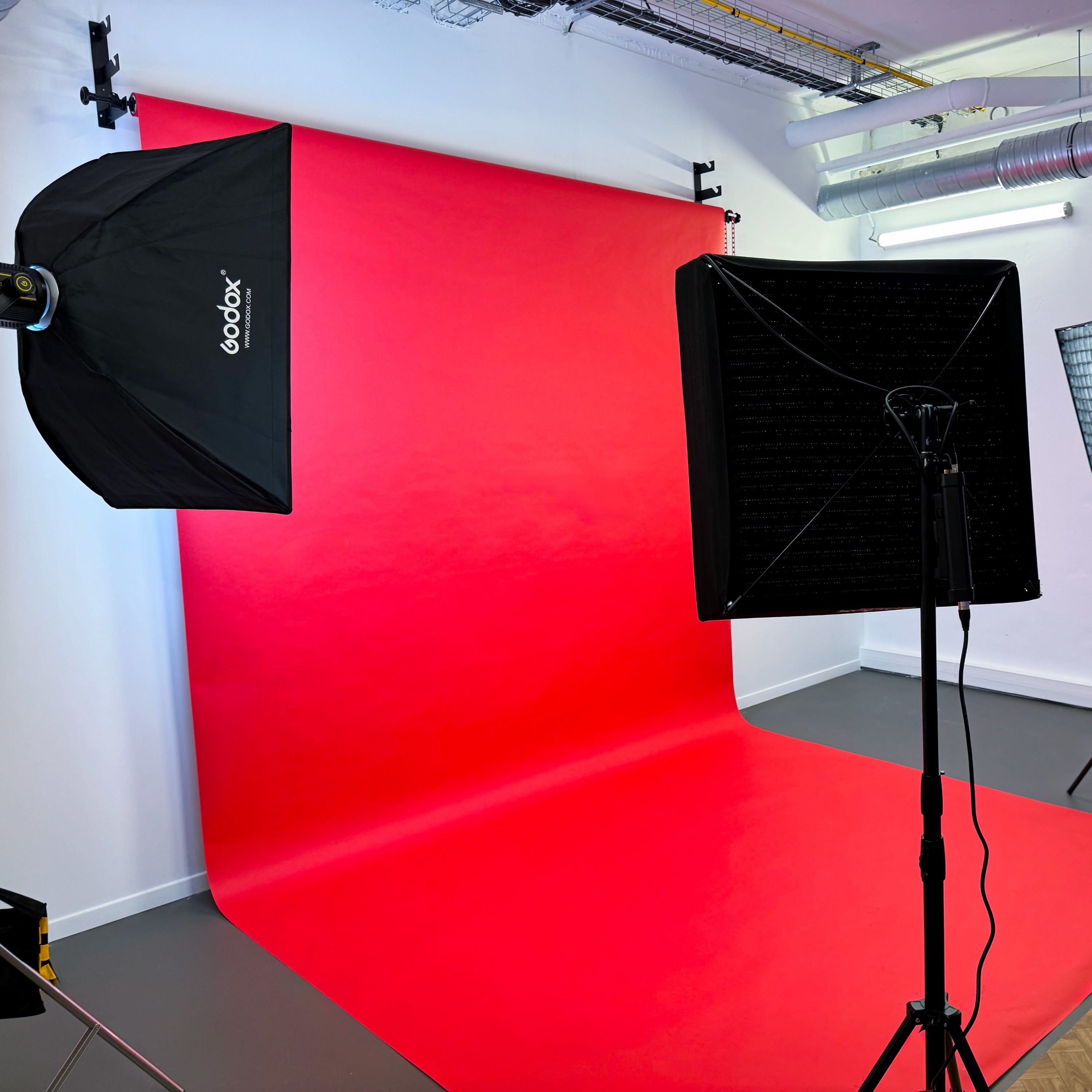 A photography studio with a red backdrop, two light sources, and a camera setup.