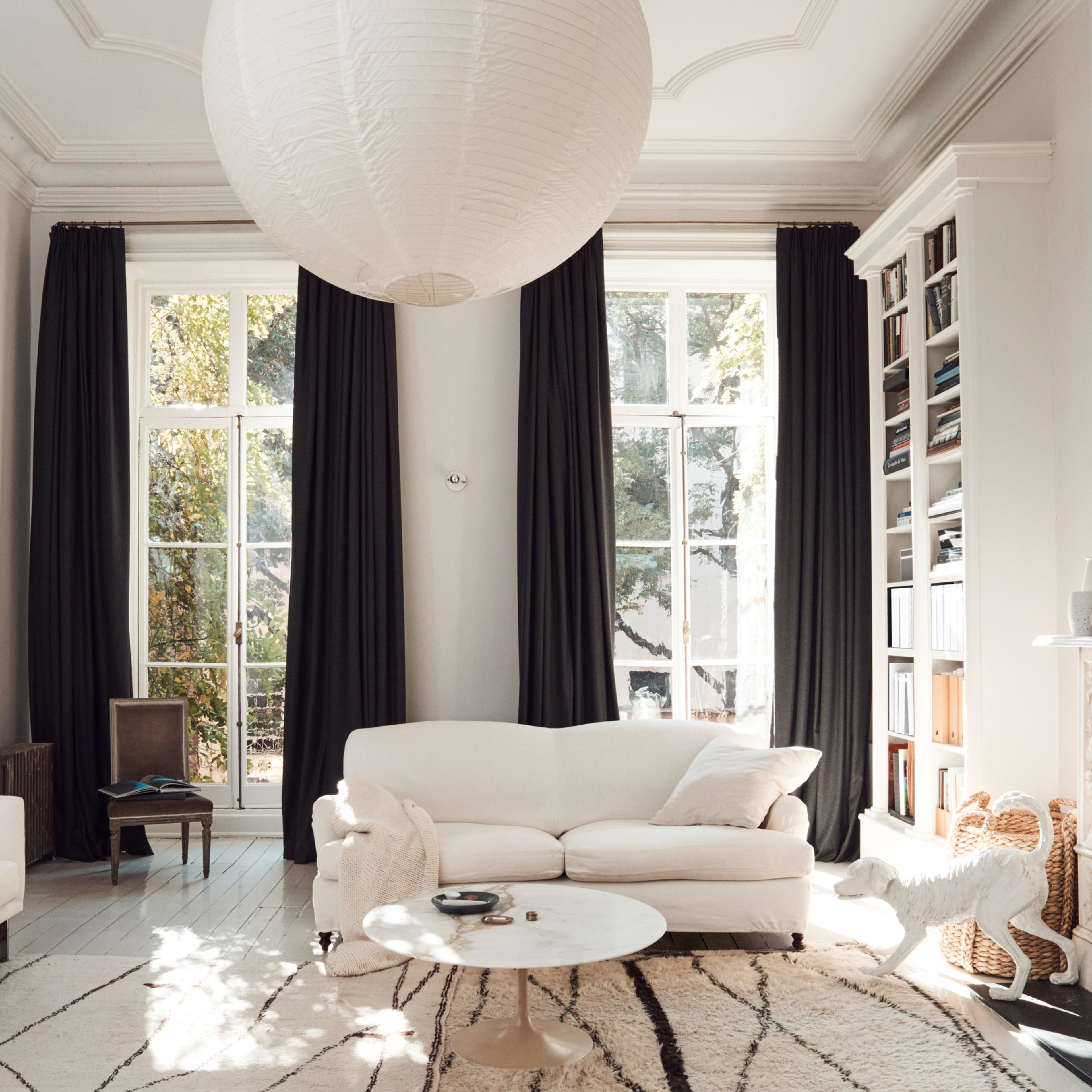 A bright living room with large windows, a white sofa, a marble coffee table, and bookshelves against the wall.