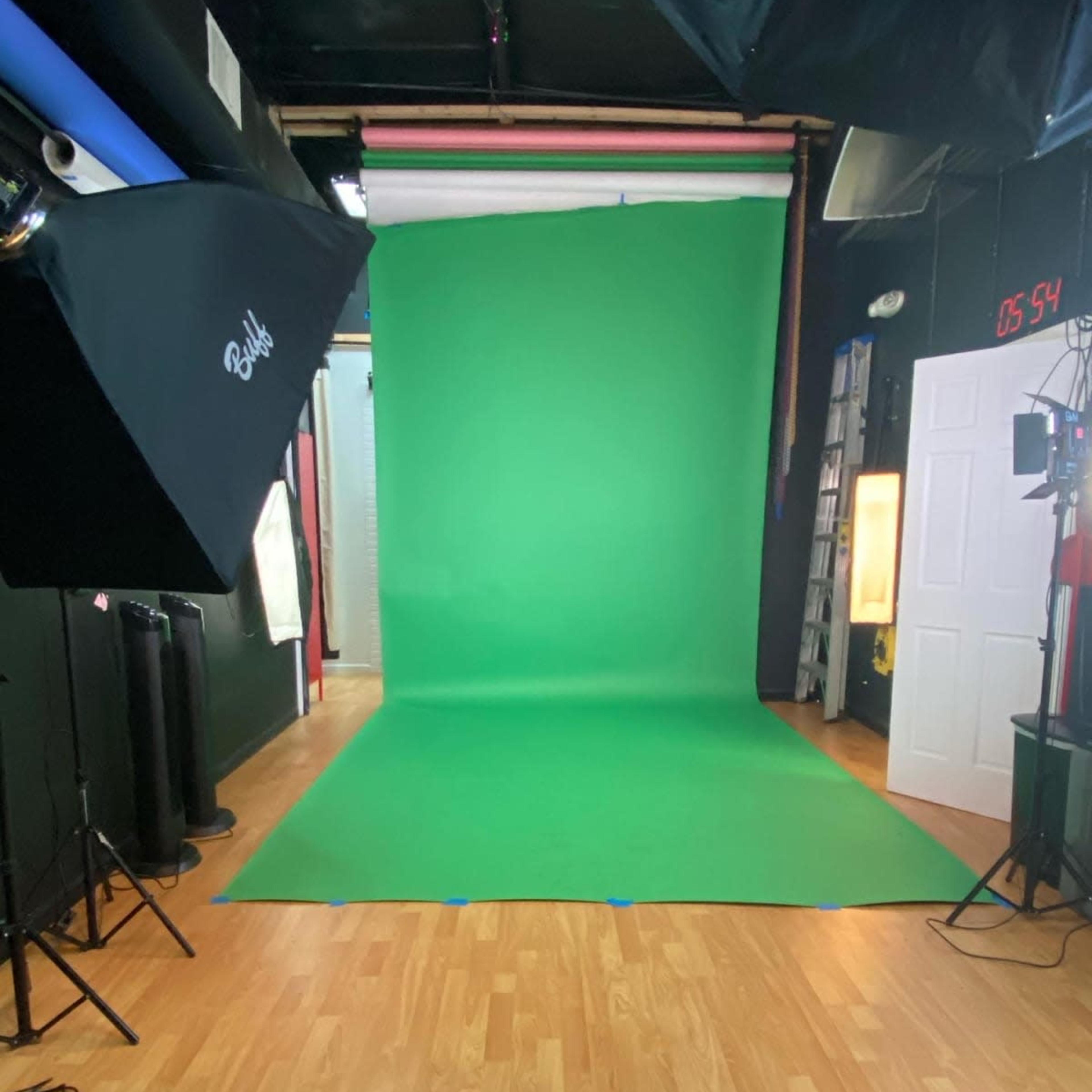 A photography studio featuring a green screen backdrop, professional lighting equipment, and a wooden floor.