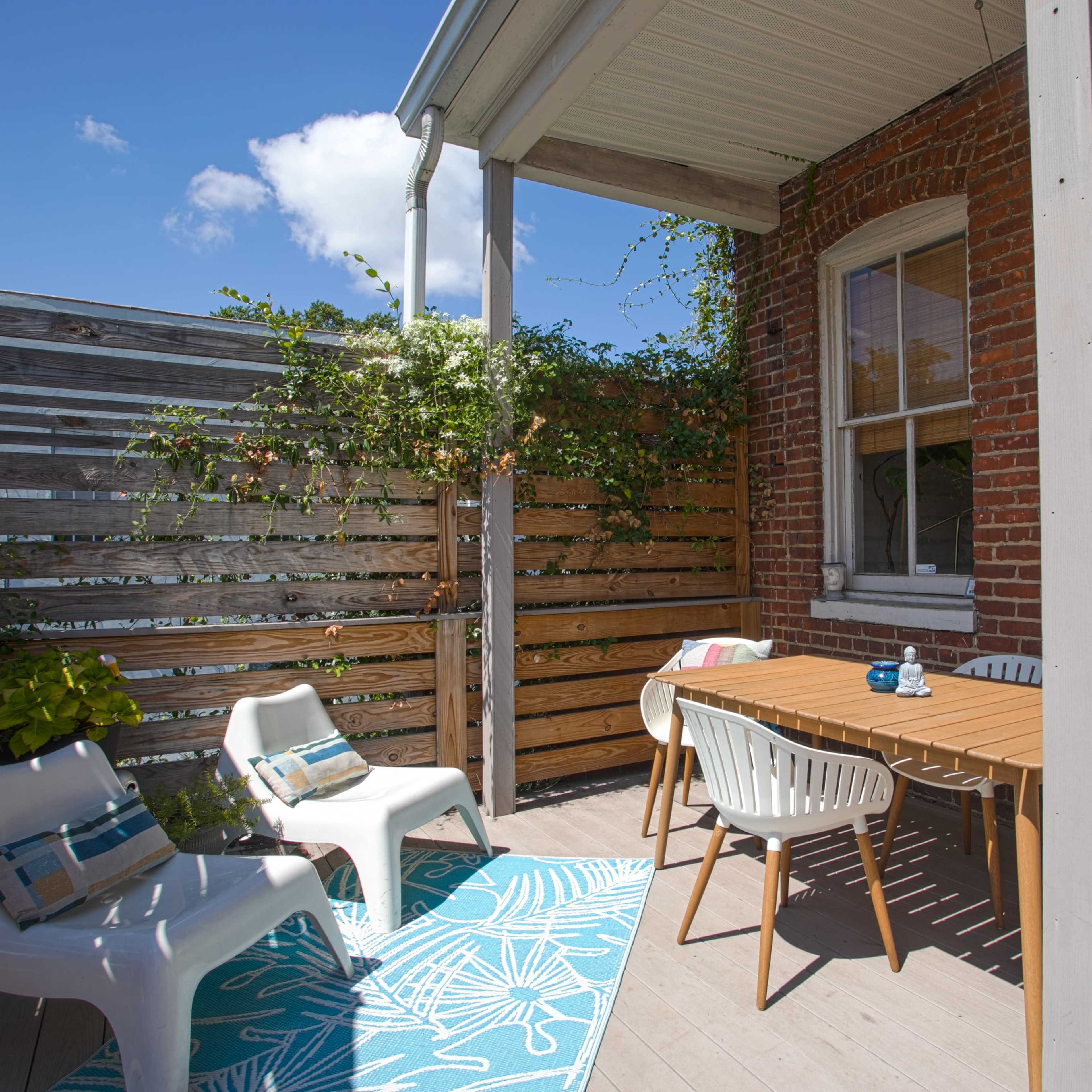 A patio area with a wooden table, chairs, and decorative plants enclosed by a wooden fence and brick walls.