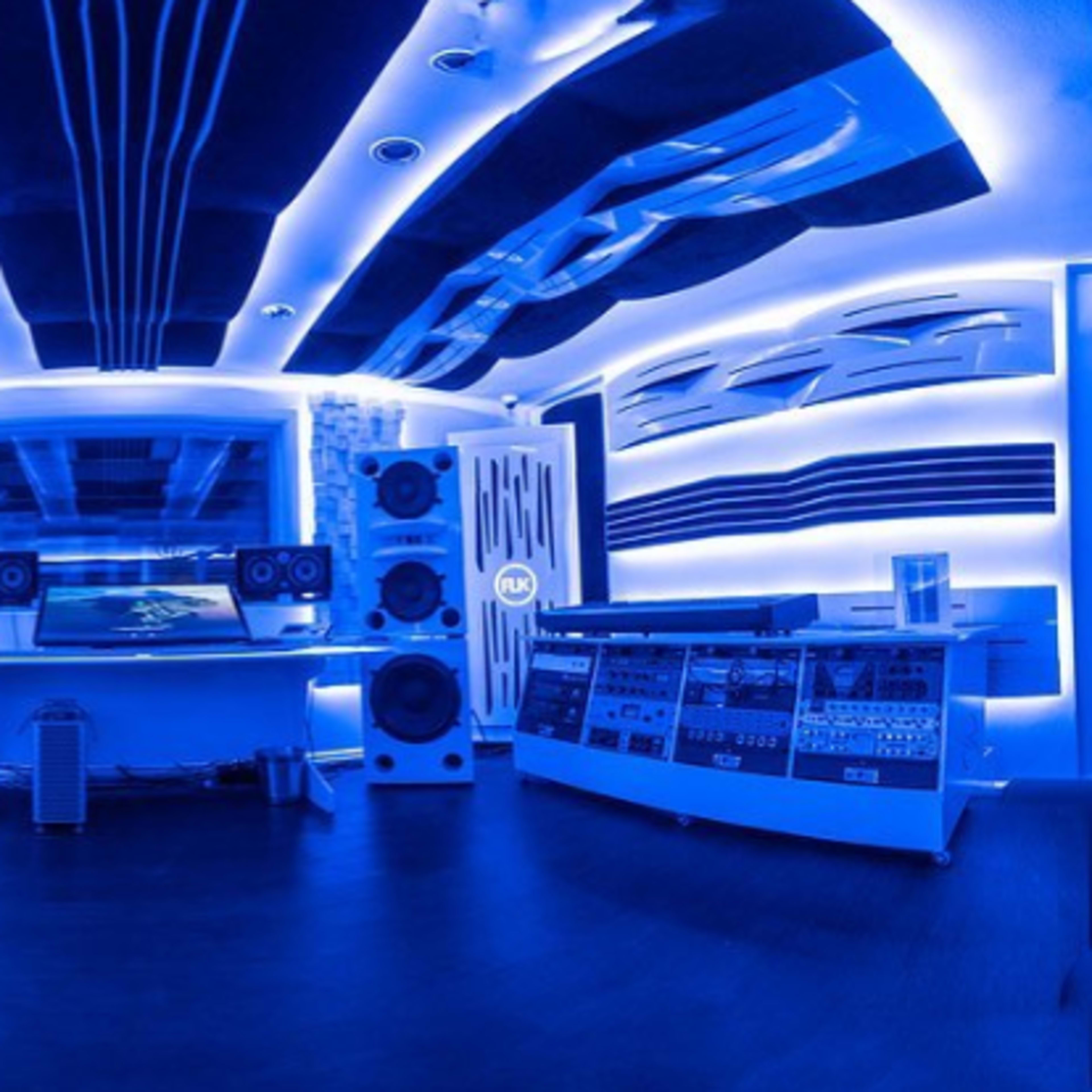 A modern music studio with blue ambient lighting, featuring large speakers and soundproofing panels on the walls.