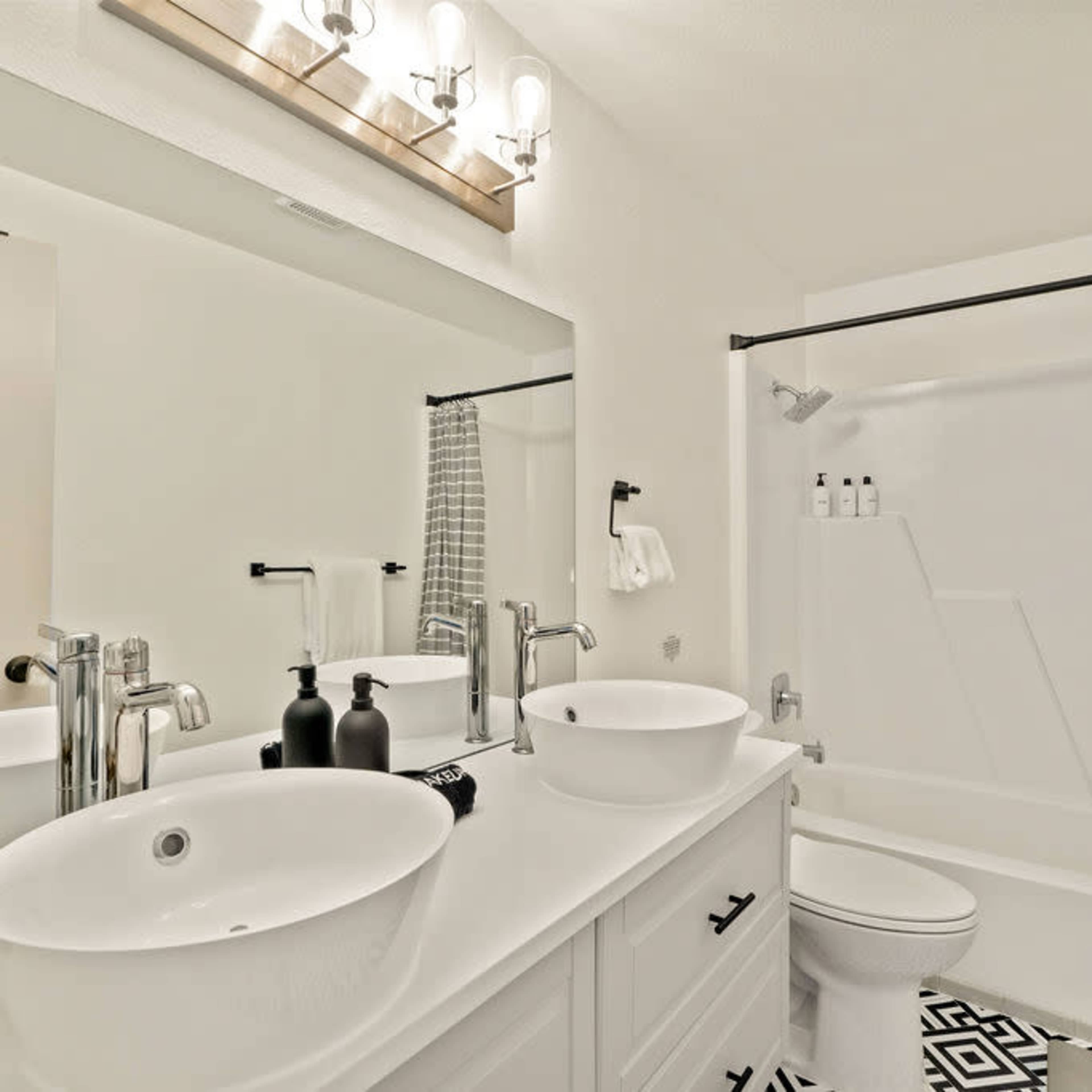 A modern bathroom featuring a double sink vanity, a bathtub with a shower curtain, and a monochrome geometric tile floor.