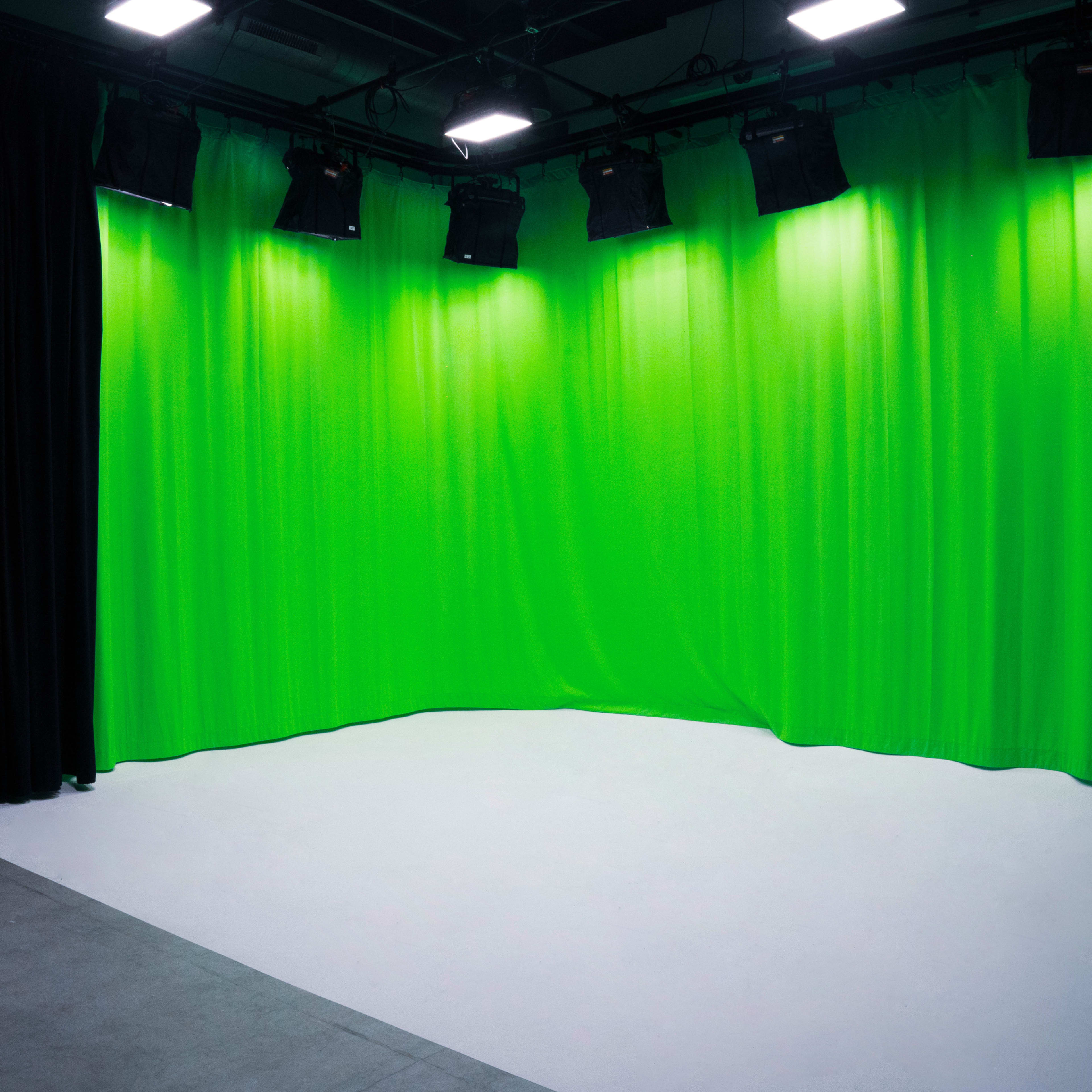 A studio with green curtains, several overhead lights, and a white floor, creating a backdrop for video production.