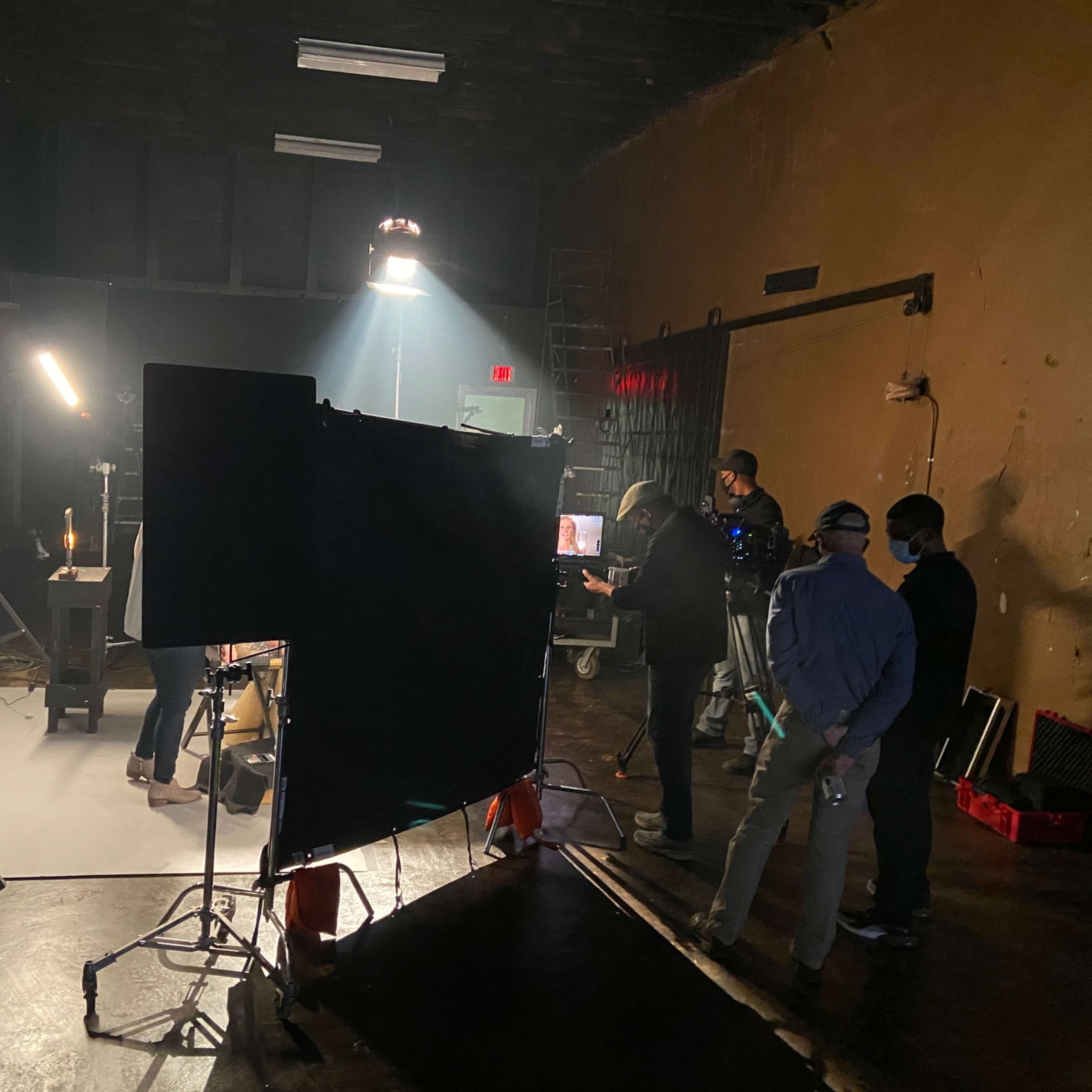 A group of people set up equipment in a studio for a photoshoot, with a backdrop and lighting rig in place.