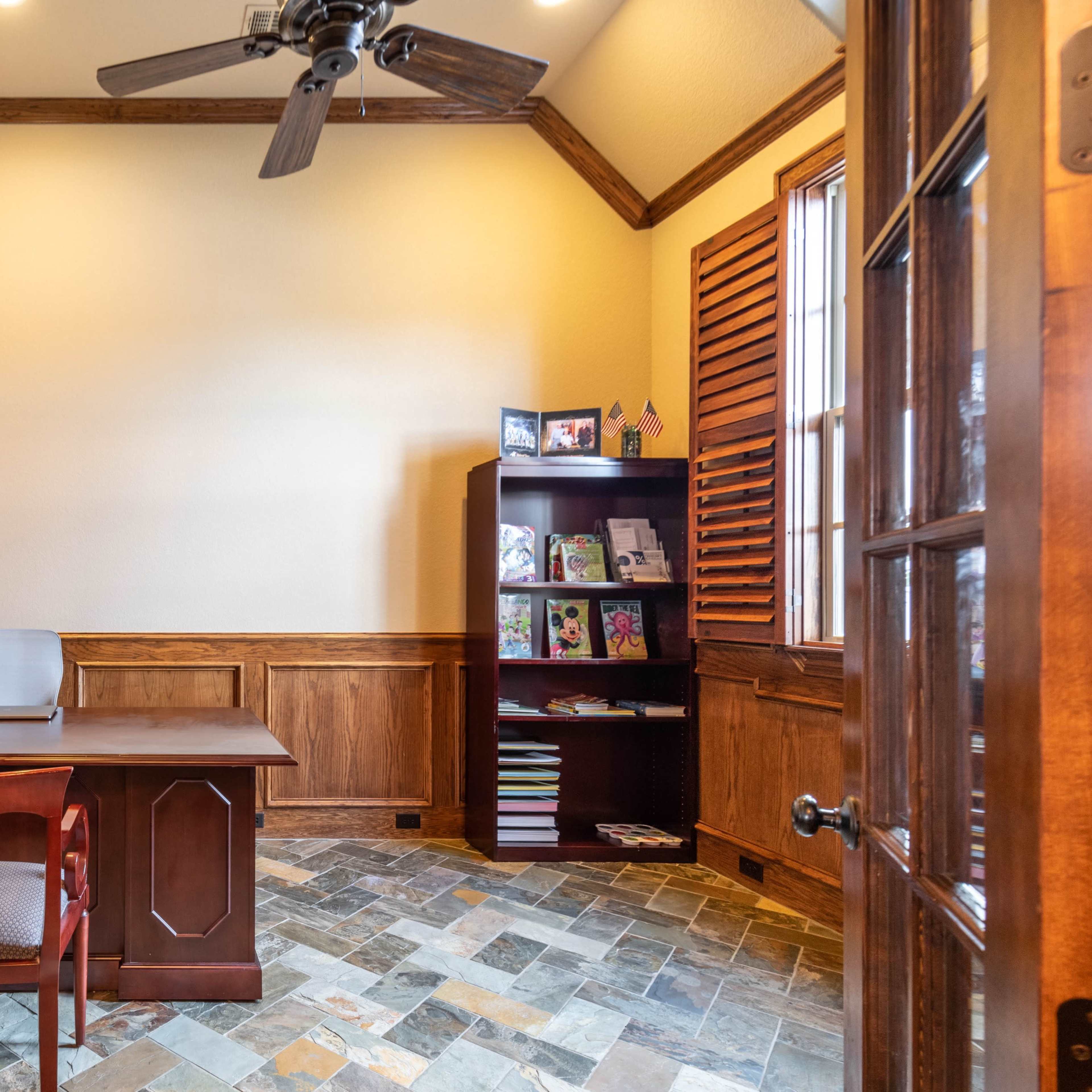 A home office with wooden paneling, a desk with a computer, and a bookshelf filled with various items.