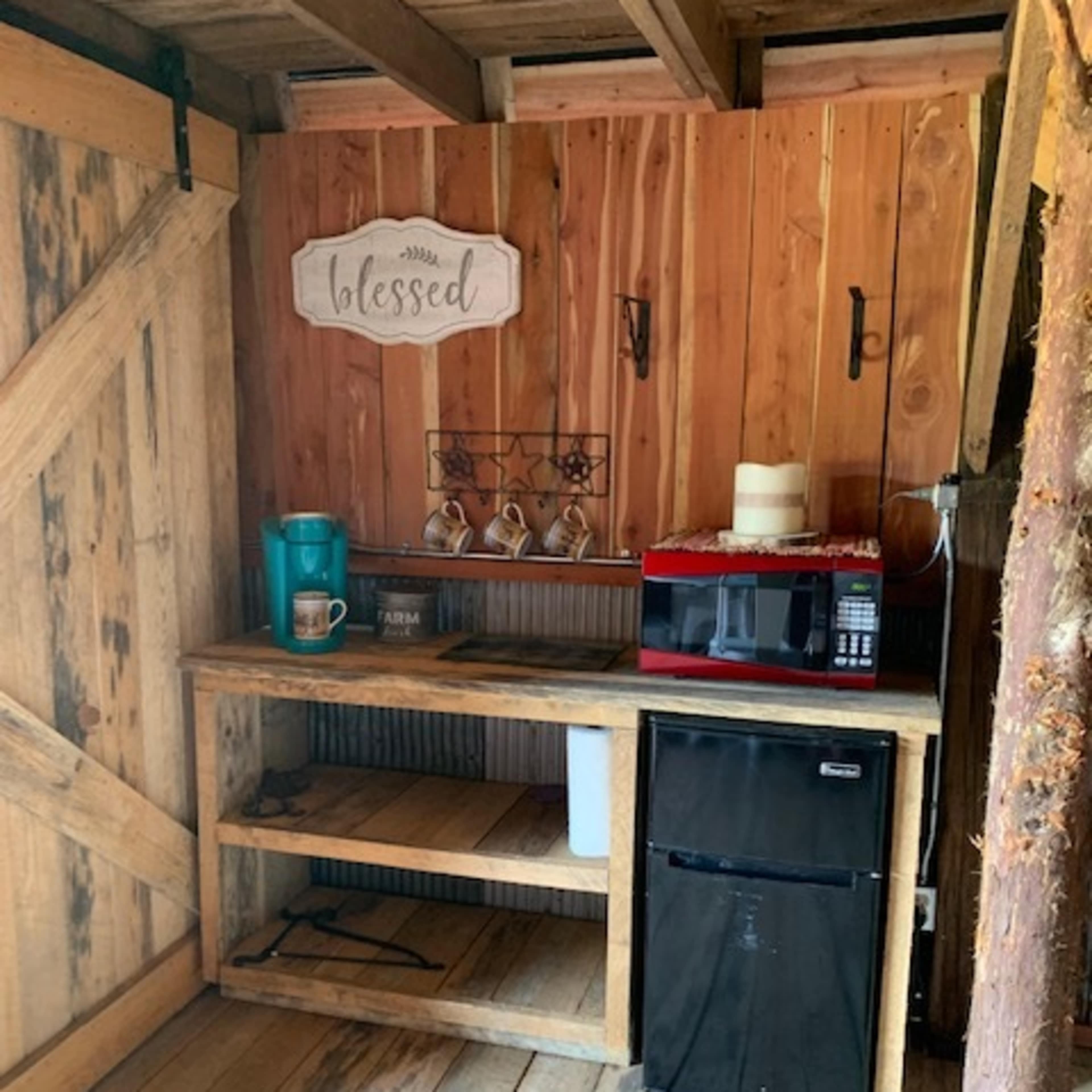 A small wooden kitchenette with a countertop, coffee maker, mini refrigerator, and a decorative sign that reads "blessed" on the wall.