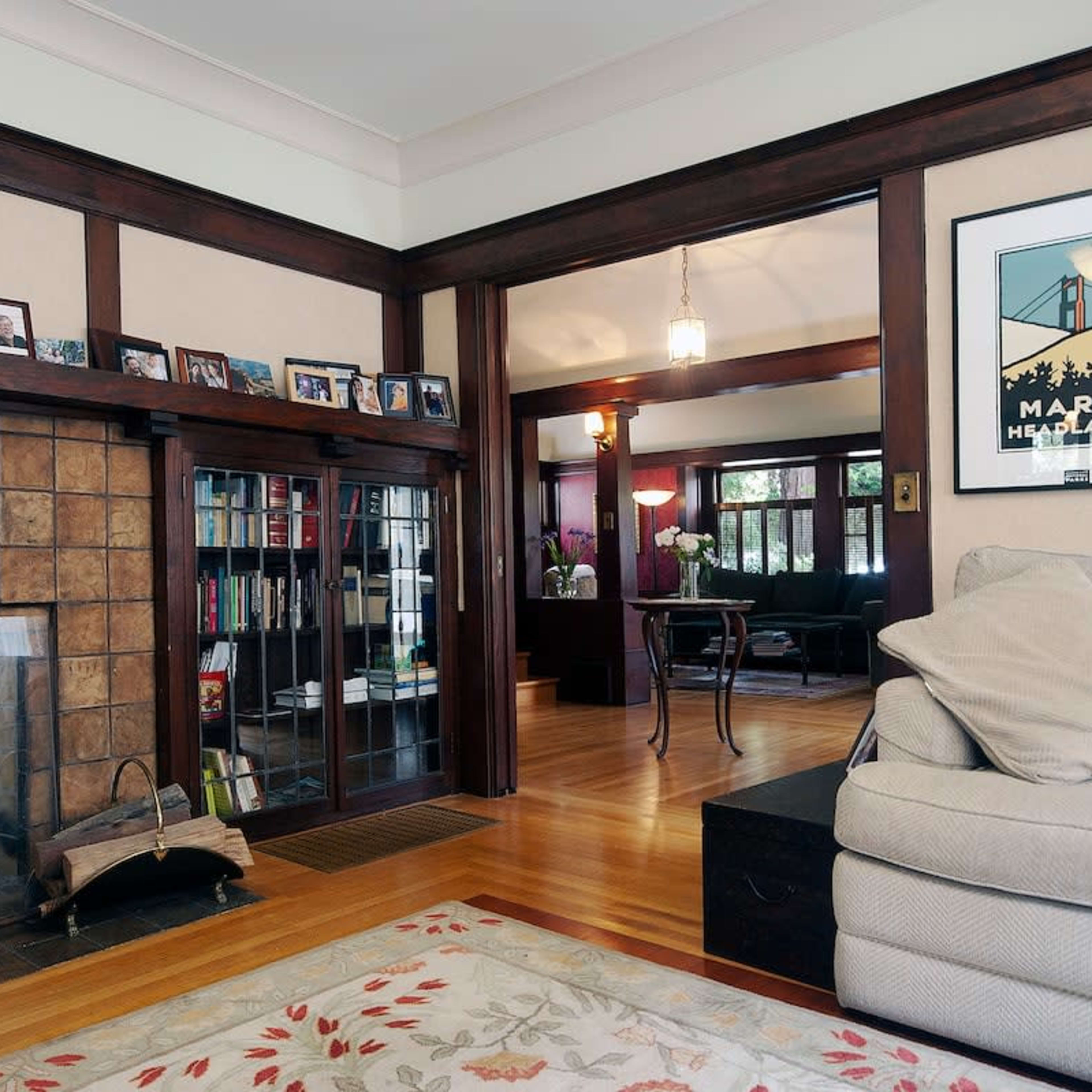 A cozy living room with a stone fireplace, bookshelves, and a large sofa, leading to another room in a home.