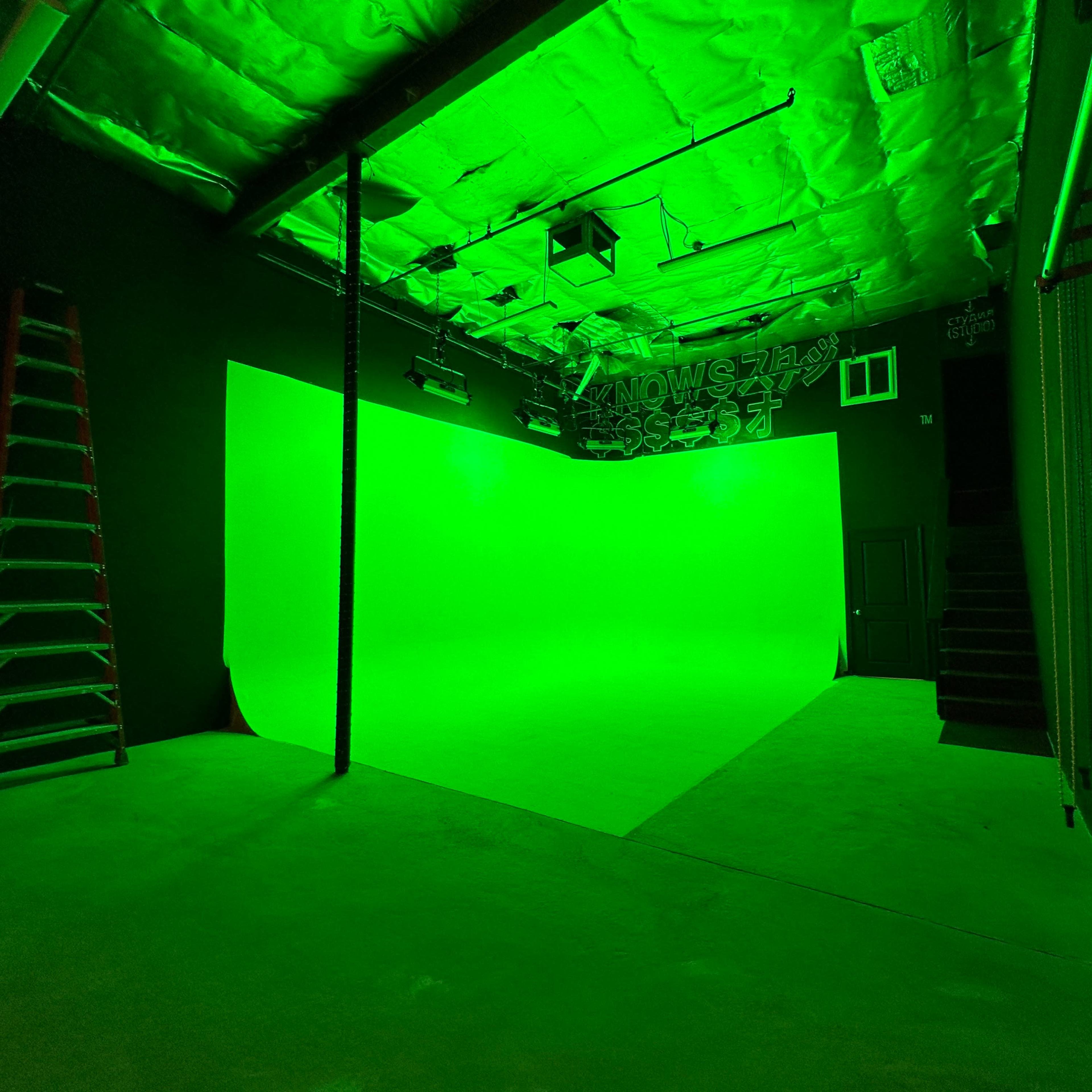 A studio space featuring a large green backdrop with a ladder and stairs in the background.