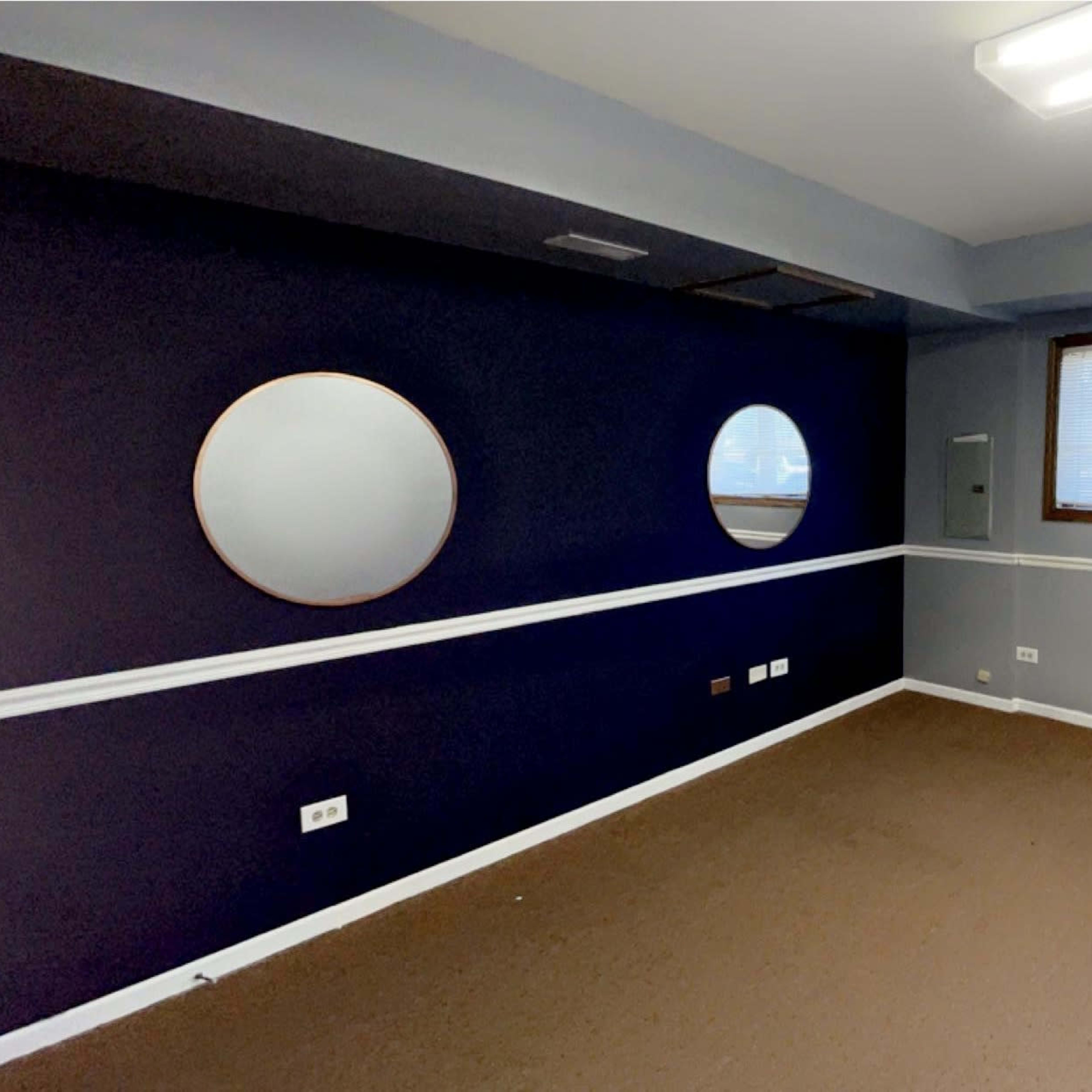 An empty room with dark blue walls, two circular mirrors, and a door leading to an outside area.