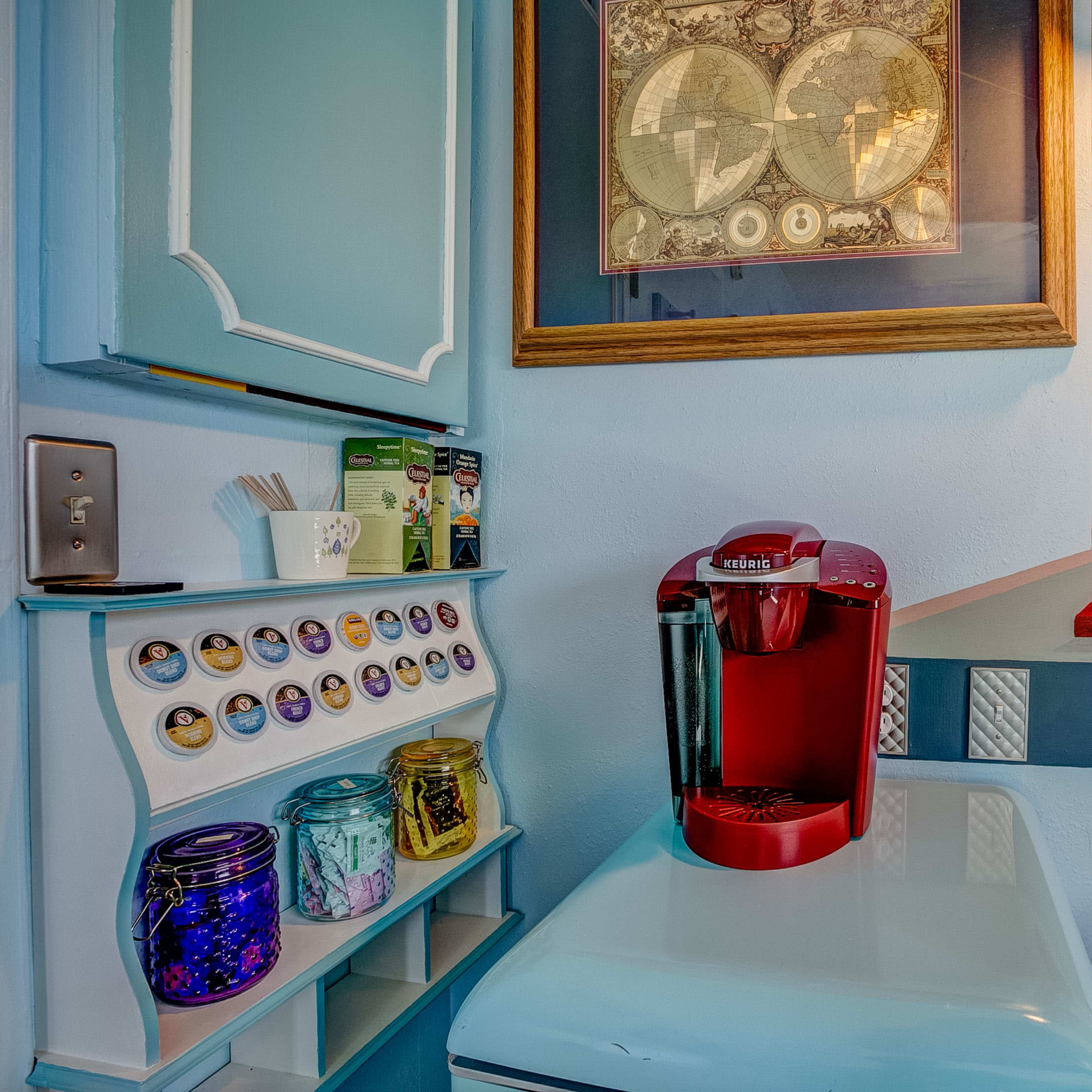 A small room with a retro-style blue wall, a red coffee machine on a table, and a colorful shelf displaying jars and pods.