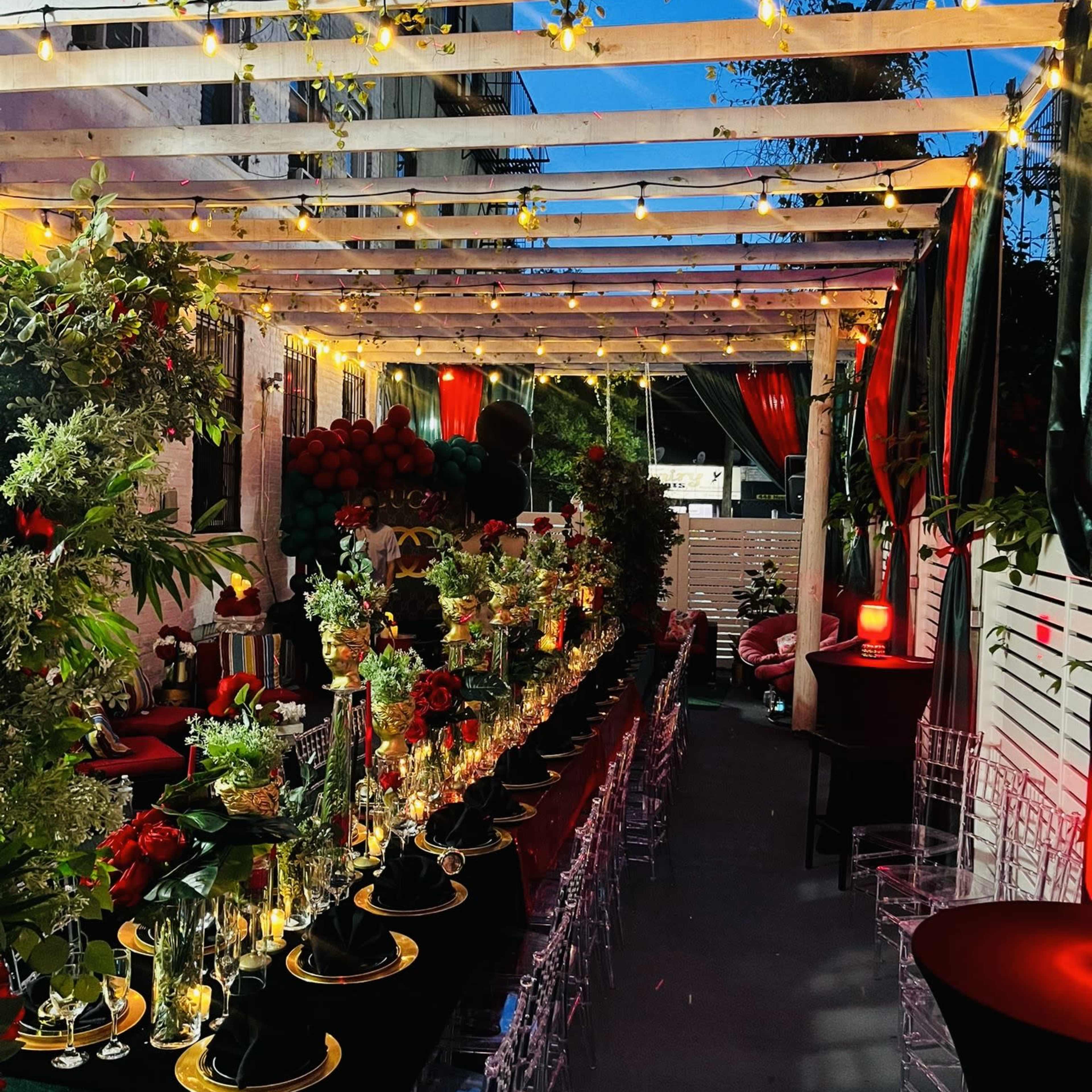 A beautifully arranged outdoor dining setup under a wooden pergola, adorned with greenery and string lights.