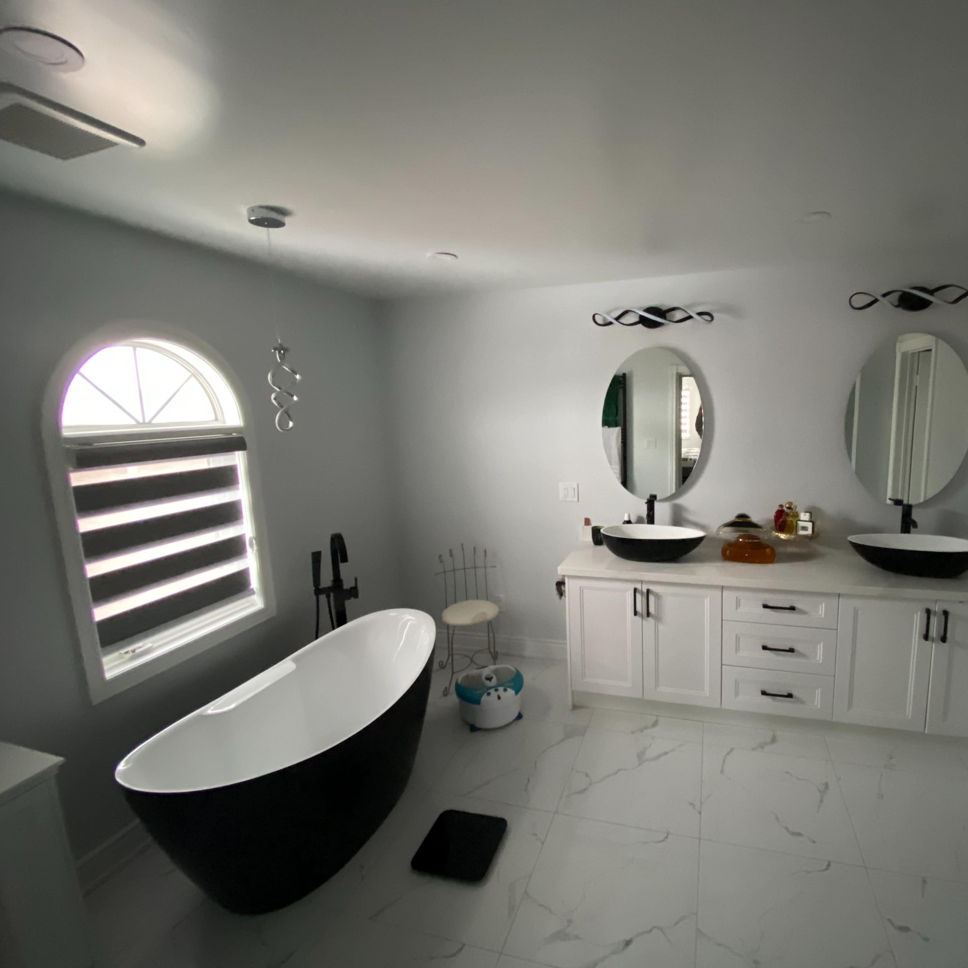 A modern bathroom featuring a freestanding black bathtub, dual round mirrors above sinks, and light-colored cabinets against a gray wall.