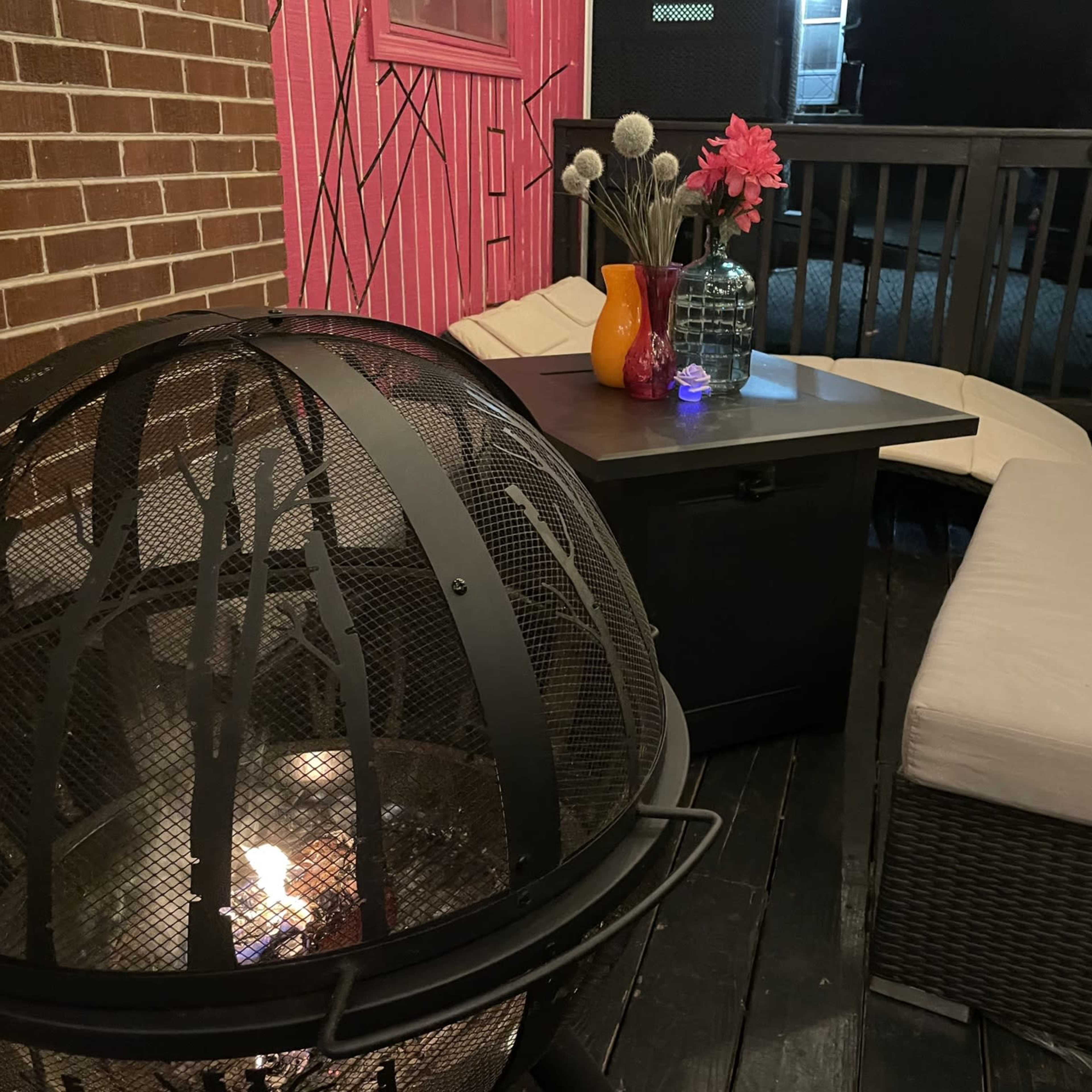 A patio area features a fire pit surrounded by seating and decorative vases on a table.