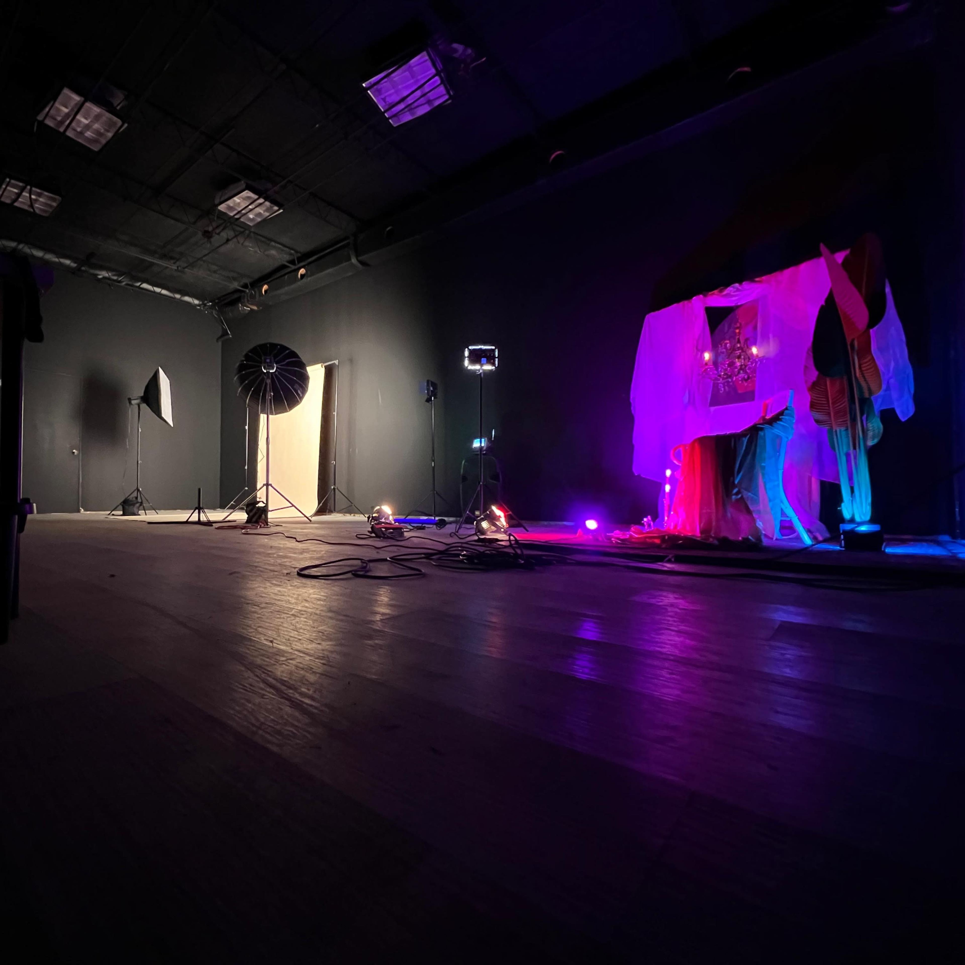 A dimly lit studio space with various lighting equipment, including a softbox and colored lights, set up for a photography session.