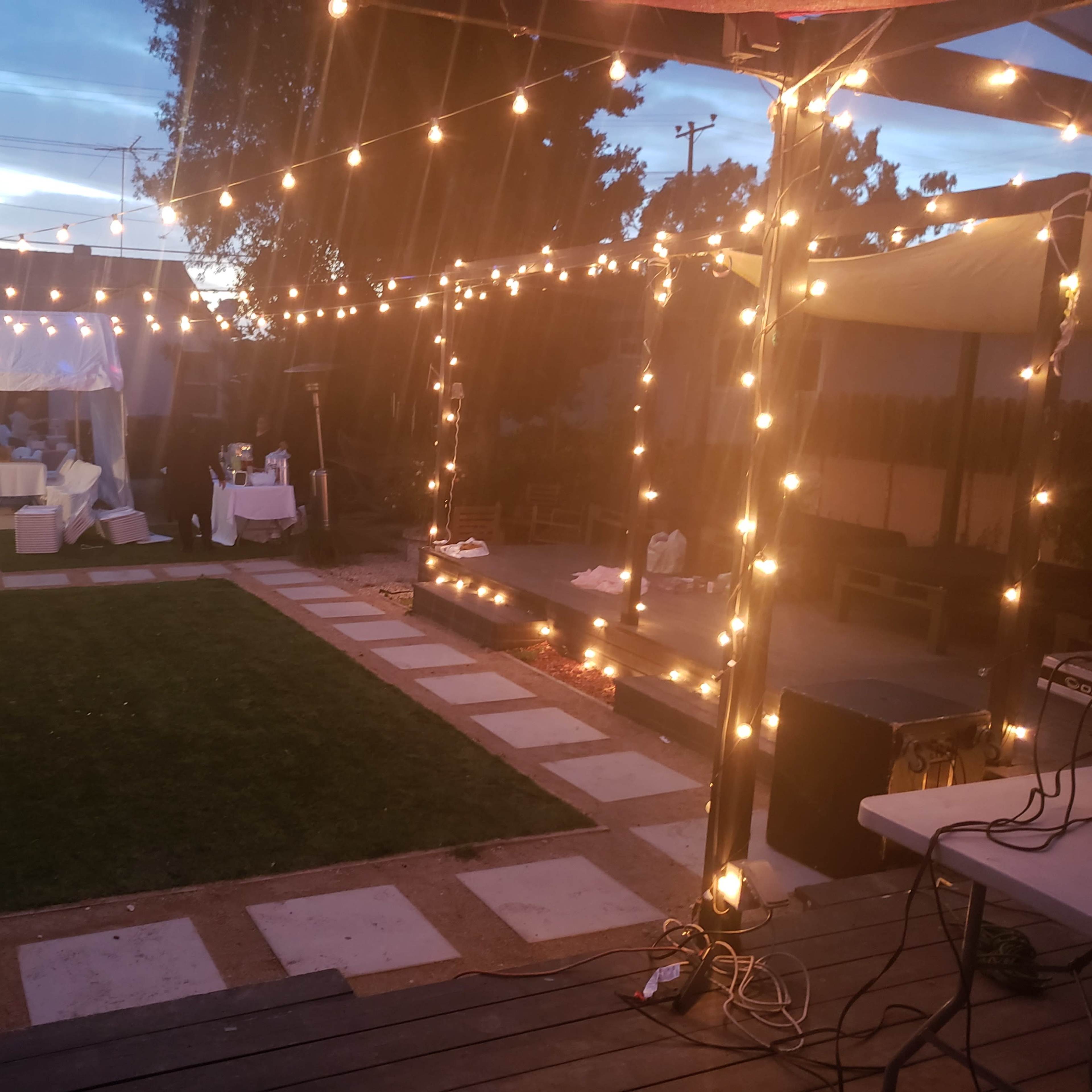 An outdoor space with string lights illuminating a patio area, a lawn, and a tent set up for an event.