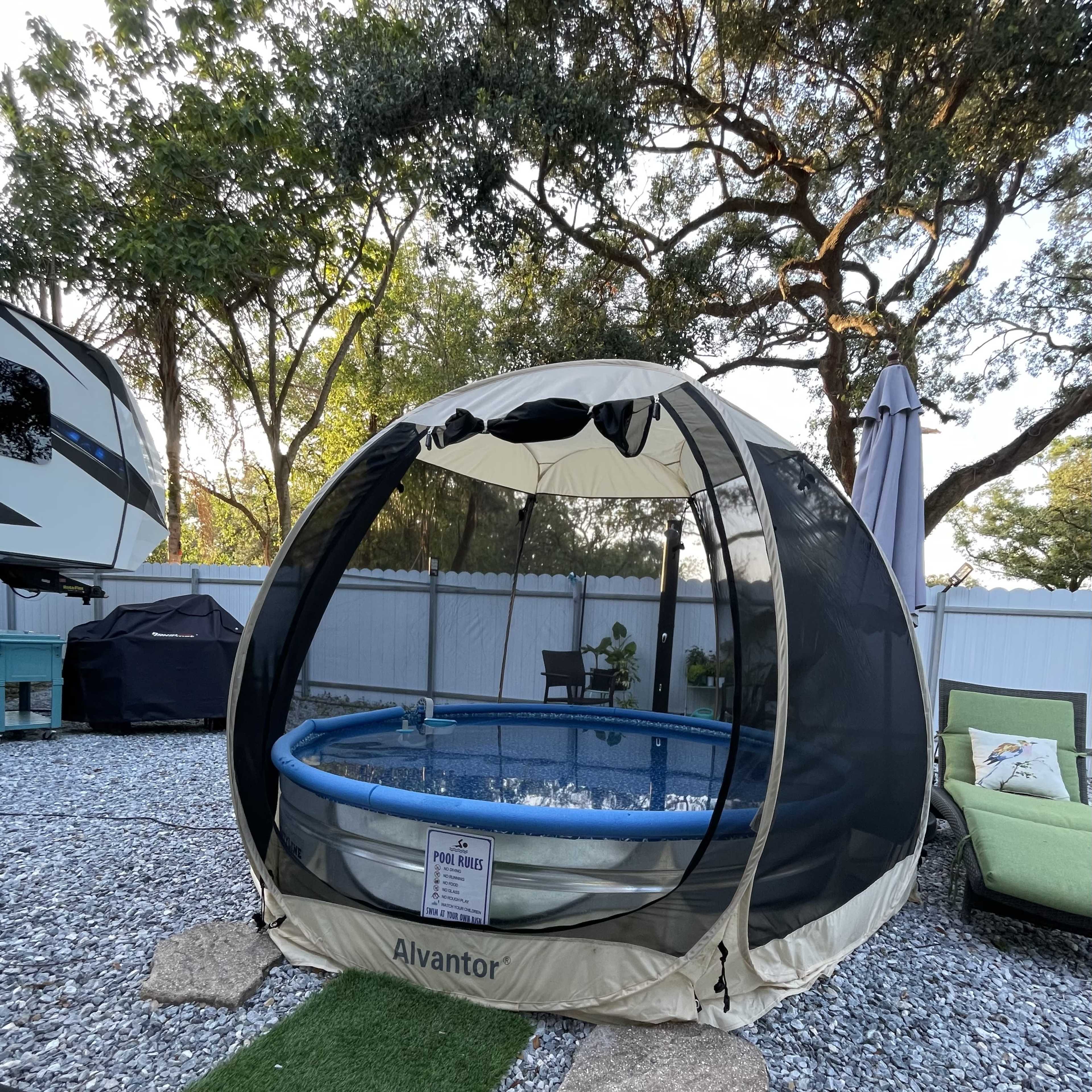 A portable pool is set up within a mesh enclosure in a backyard with gravel and greenery.