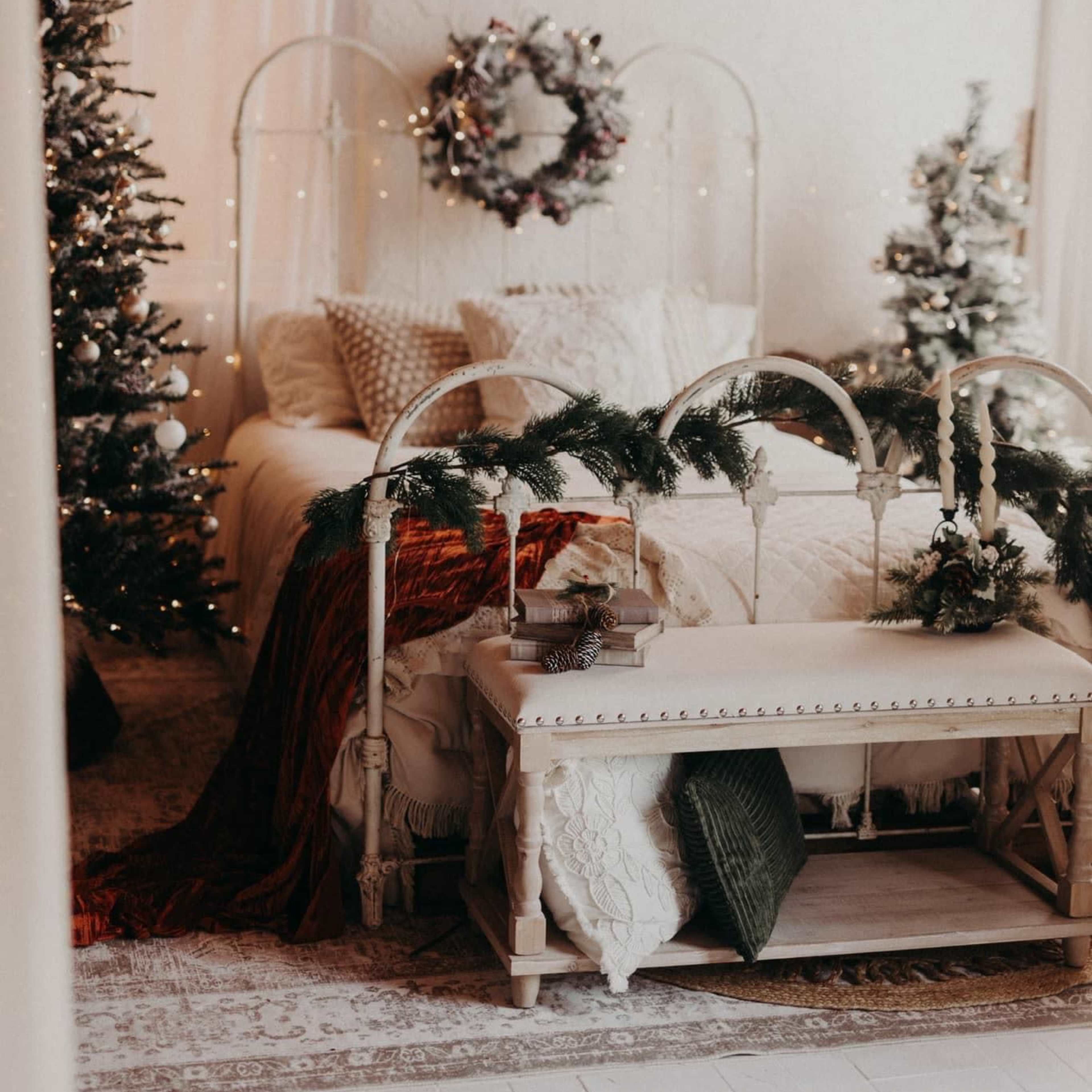 A cozy bedroom is adorned with Christmas trees, festive decorations, and a bed draped in warm blankets.
