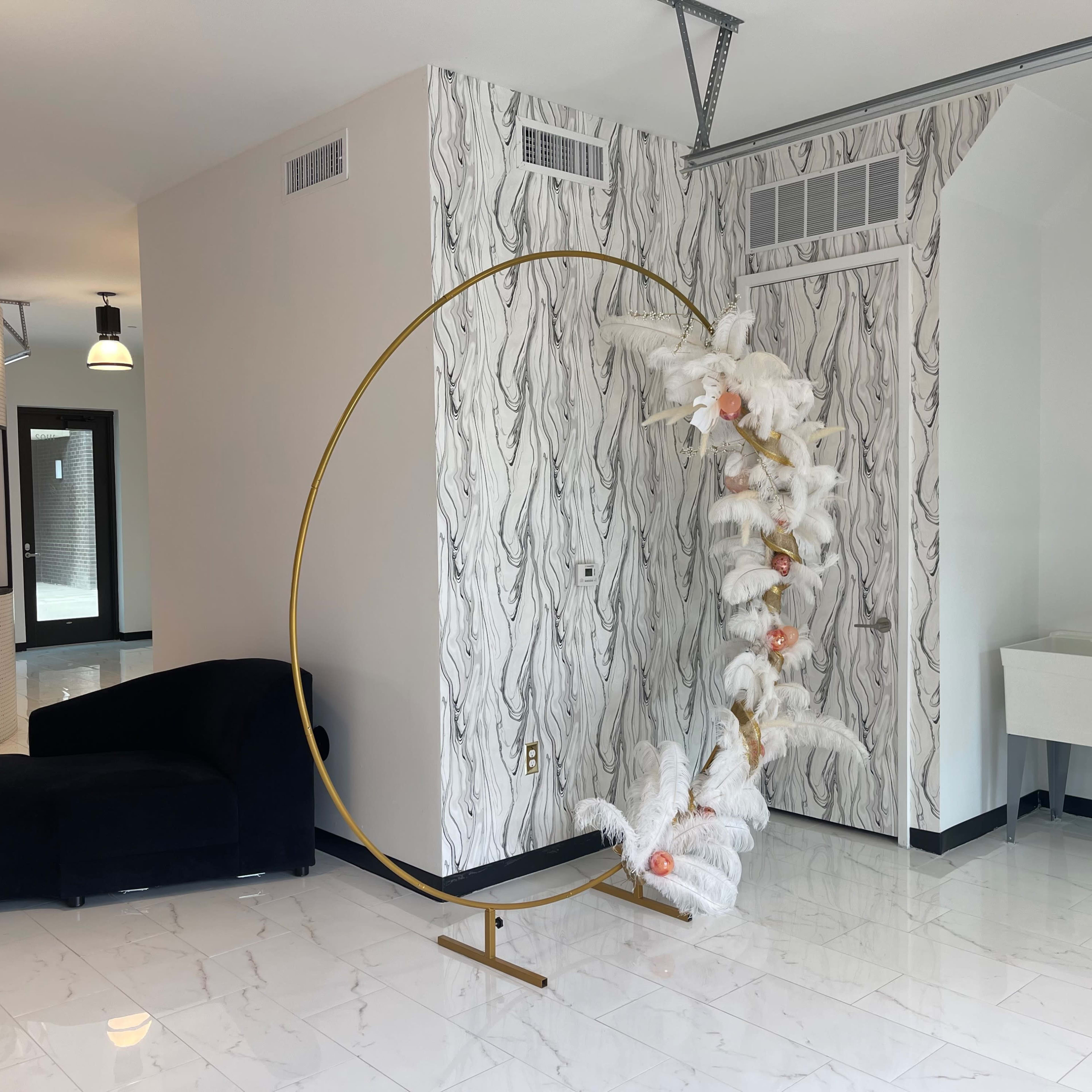 A modern interior space featuring a curved gold display stand with white decorative elements, a dark blue sofa, and a marble-tiled floor.