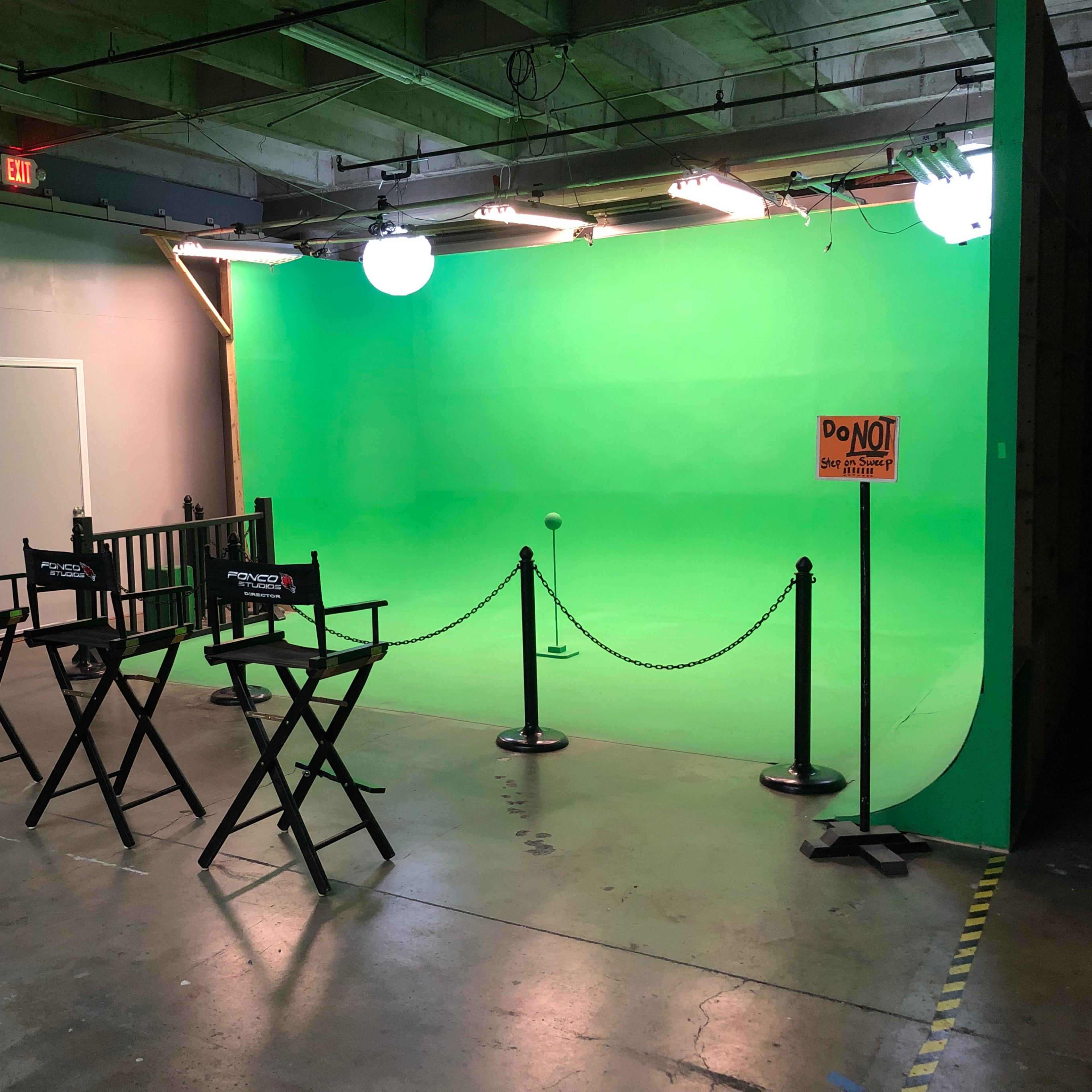 A film studio setup with a green backdrop, three director's chairs, a microphone stand, and a "DO NOT ENTER" sign.