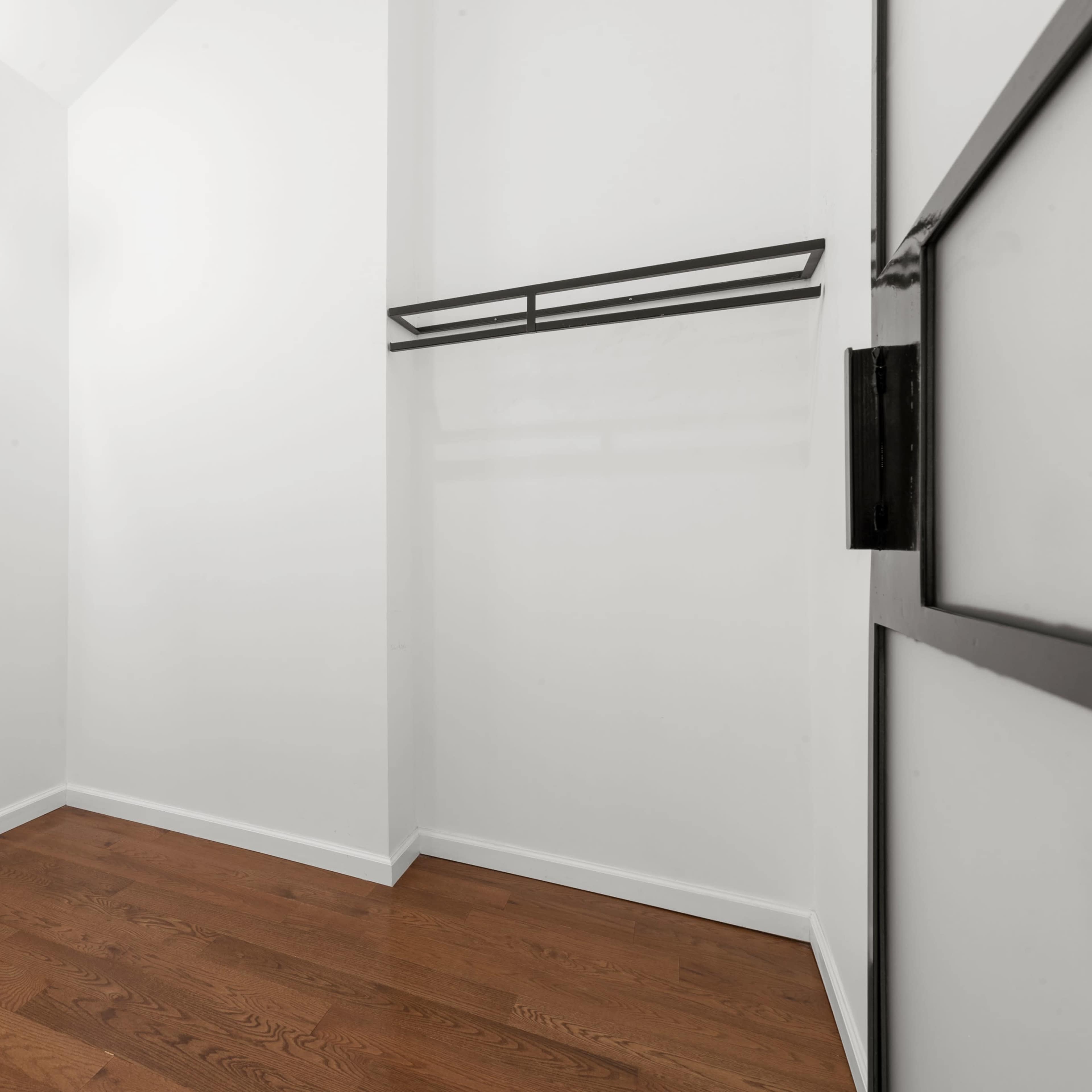 A spacious, minimalist closet featuring a large mirror, a clothing rack, and wooden flooring.