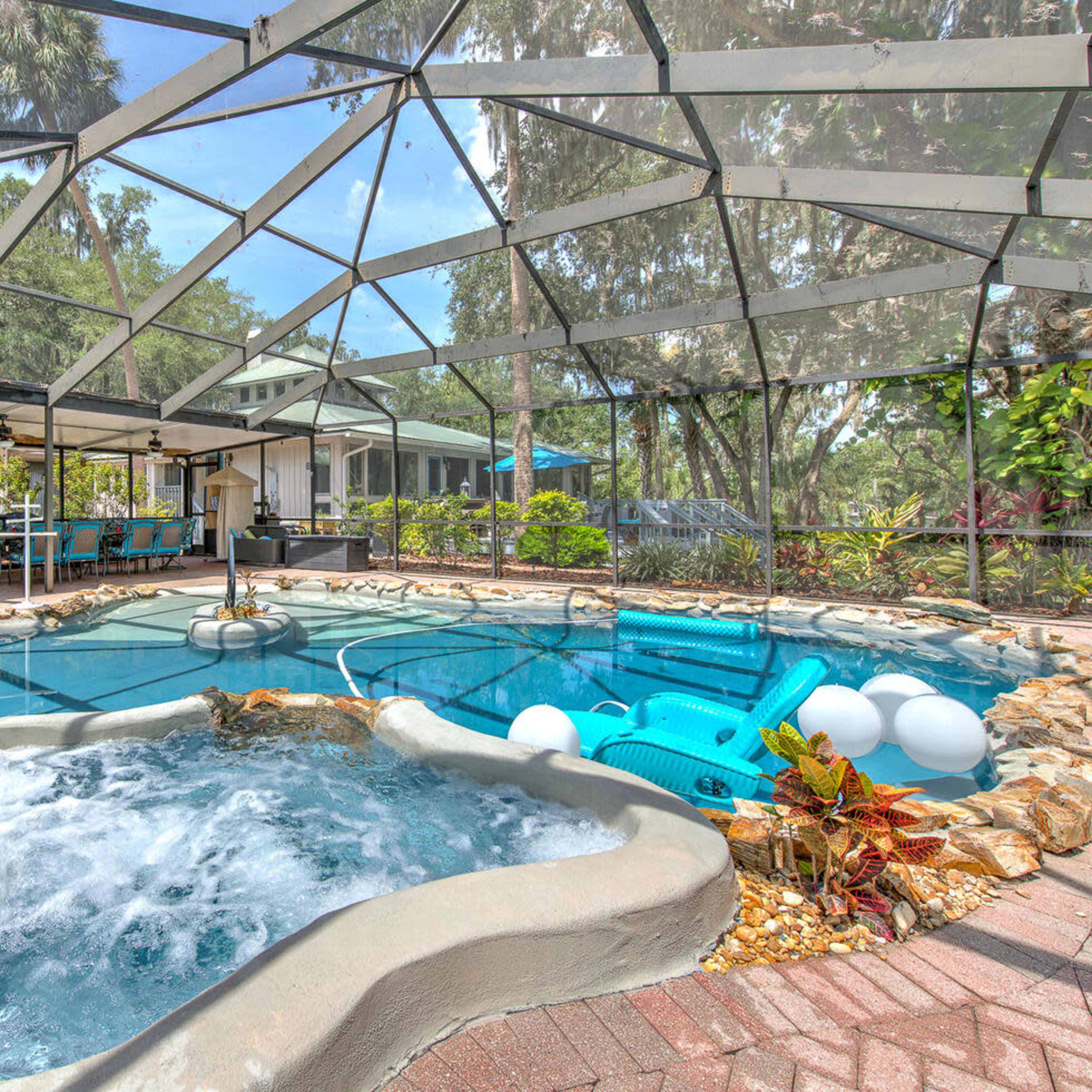 A screened-in pool area featuring a hot tub, swimming pool, and lounge seating surrounded by greenery.