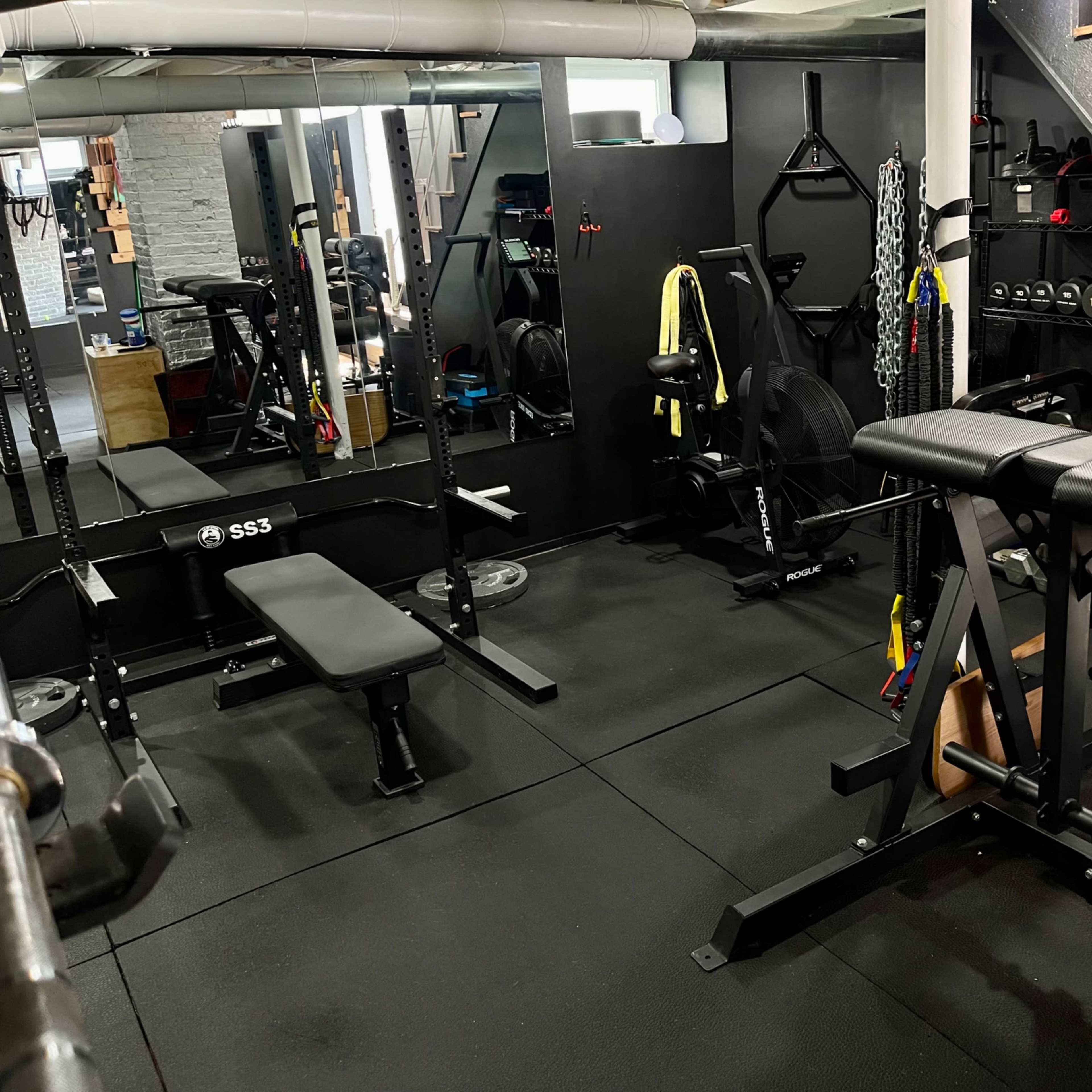 A well-equipped home gym featuring various exercise machines, free weights, and a set of stairs leading to an upper level.