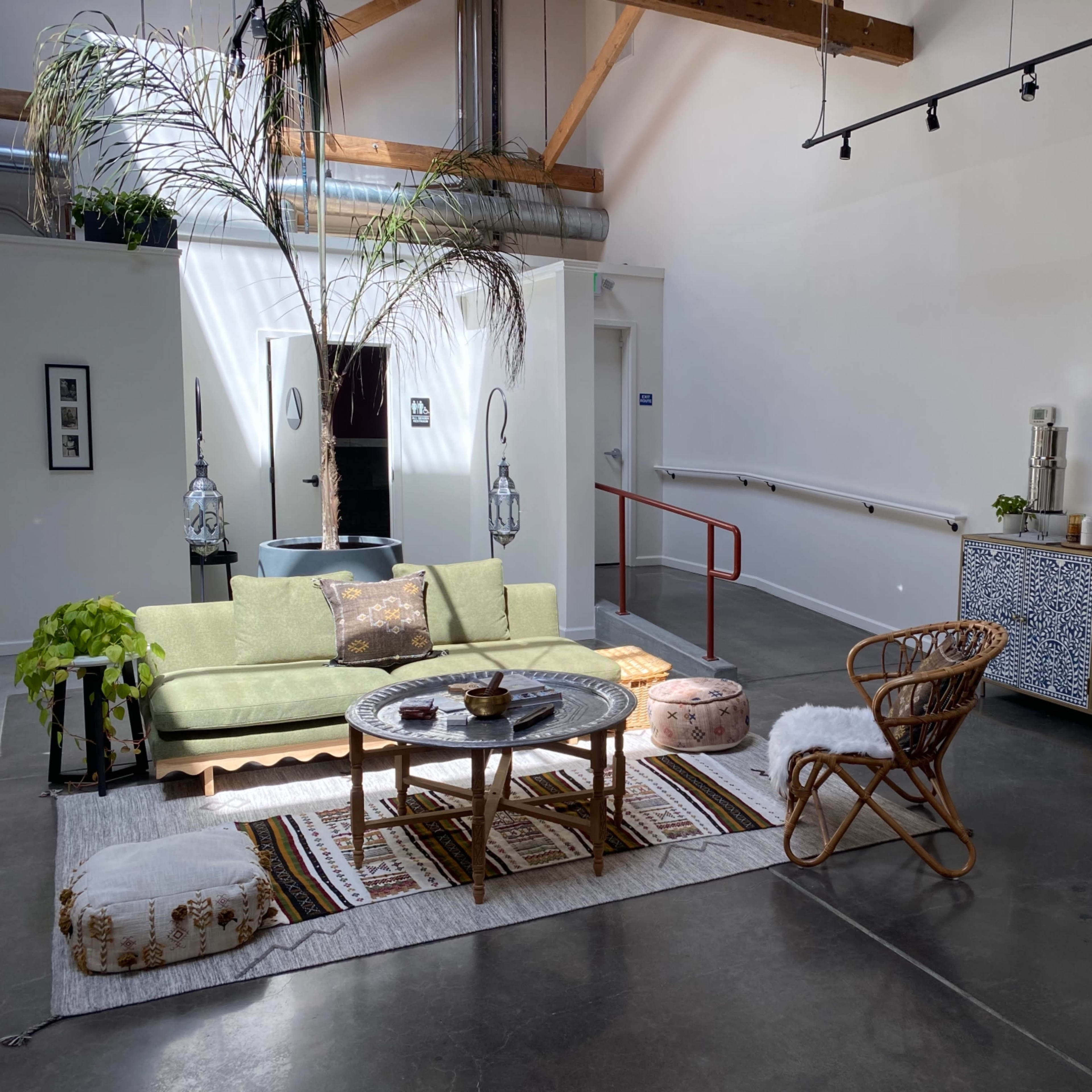 A living space features a green couch, round coffee table, patterned rug, and a woven chair, complemented by a decorative cabinet and potted plants.