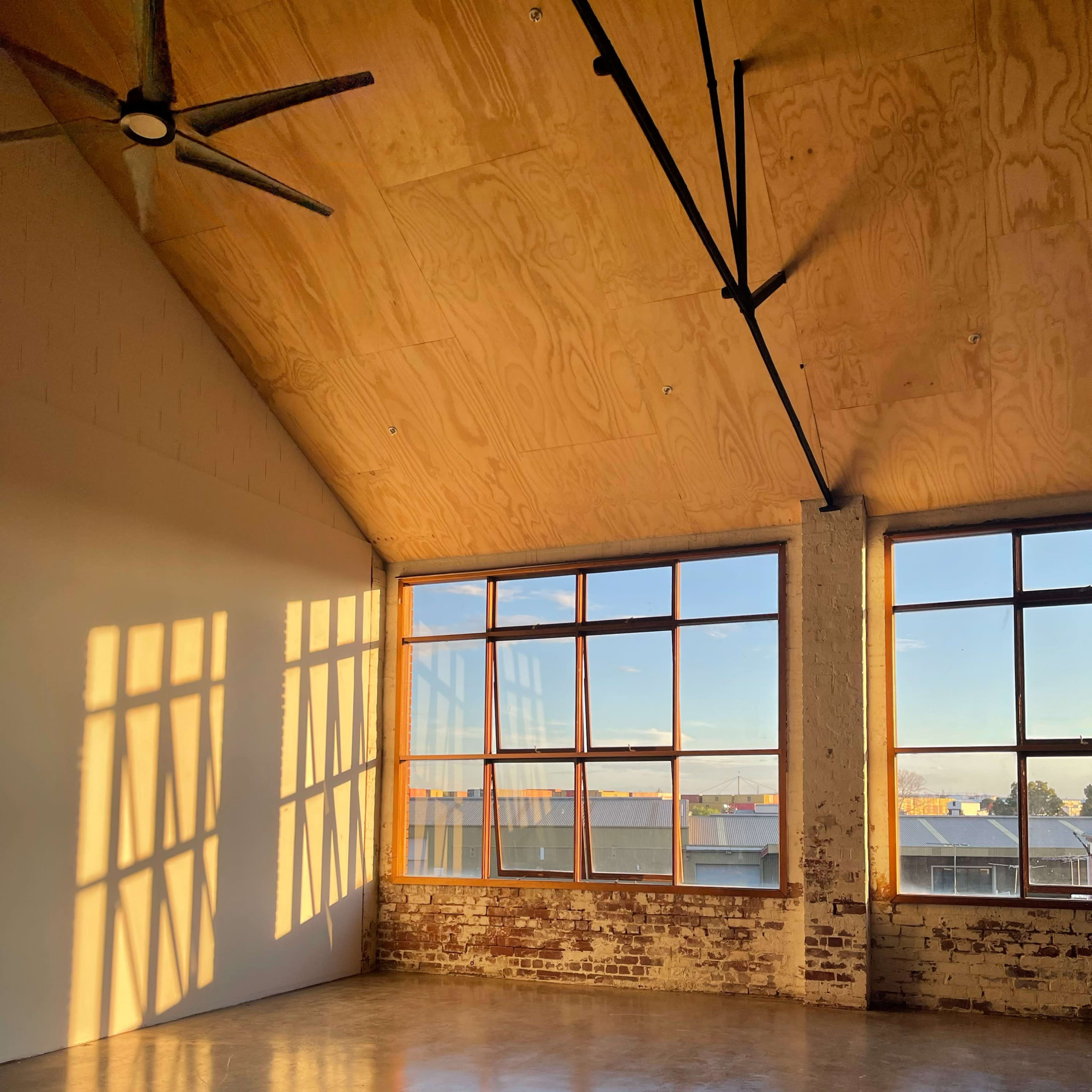An empty room with large windows allowing sunlight to cast shadows on the wall and floor.