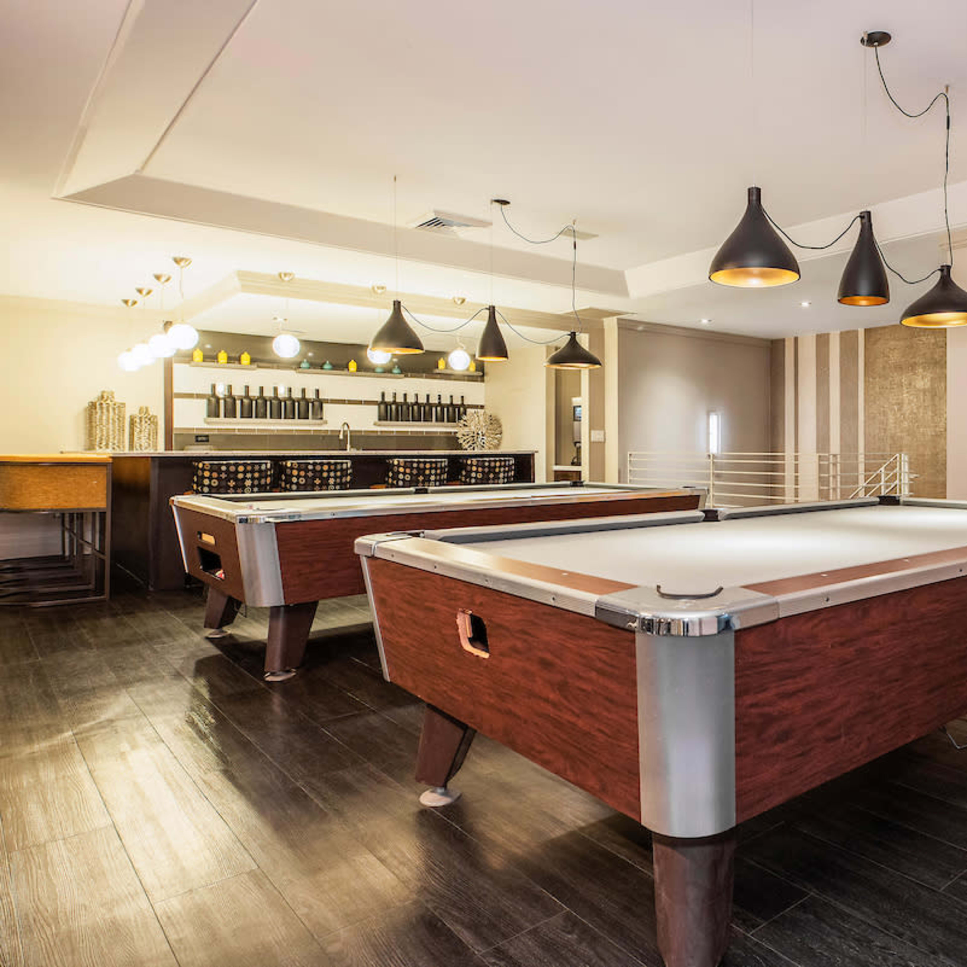 A modern game room featuring two pool tables and a bar area with pendant lighting and a colorful artwork on the wall.