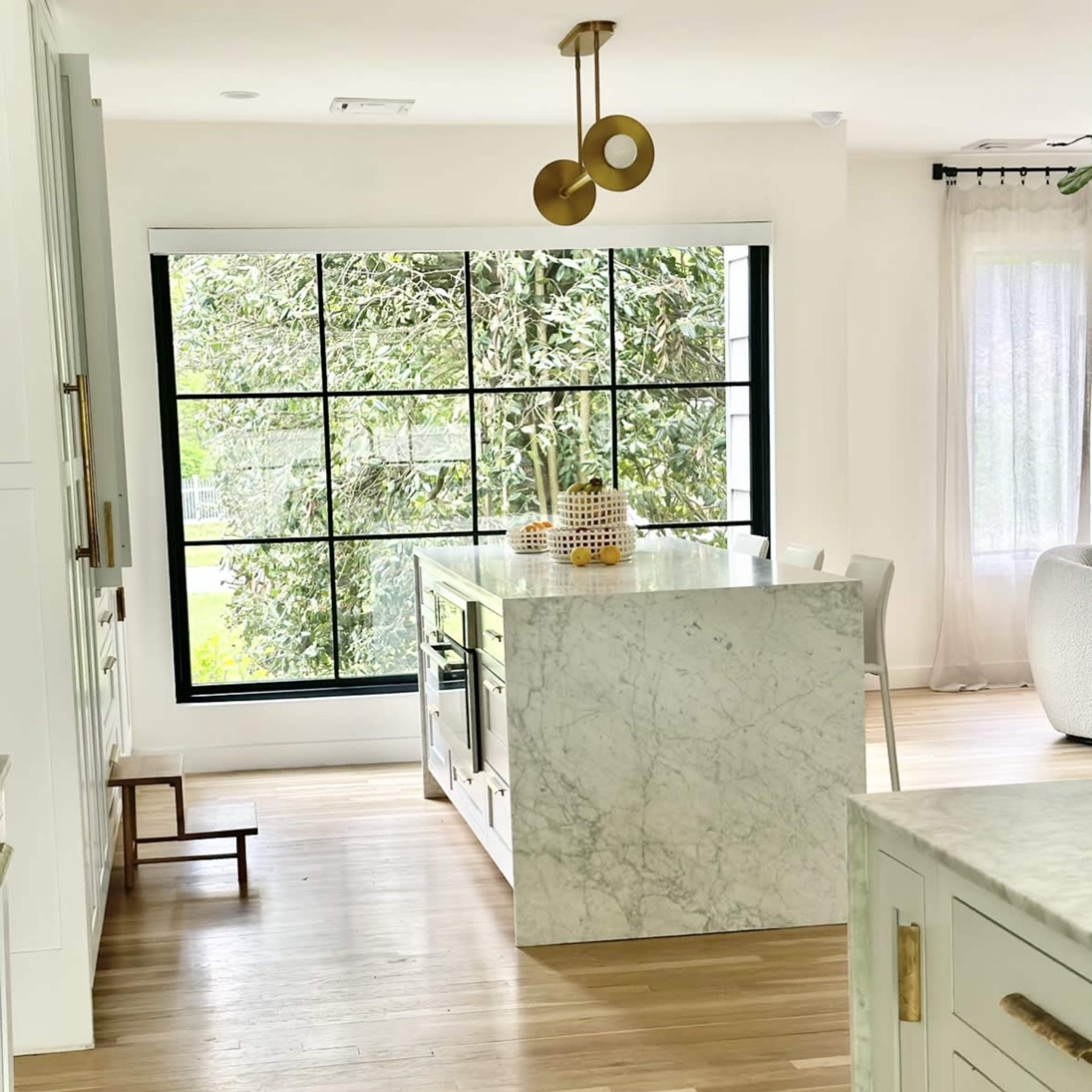 A modern kitchen features a large marble island and a spacious window overlooking greenery.