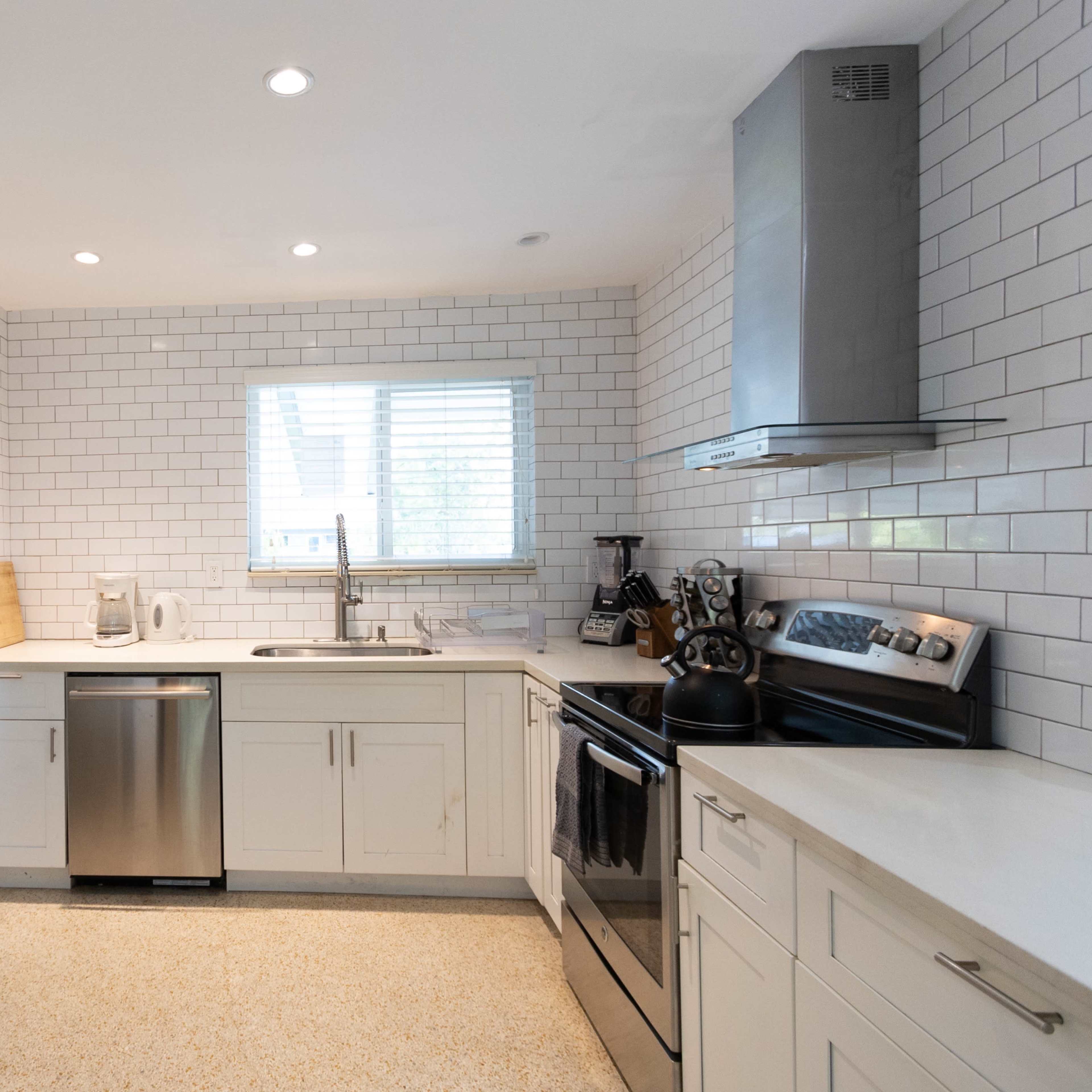 A modern kitchen featuring stainless steel appliances, white cabinetry, and a tiled backsplash with a window above the sink.