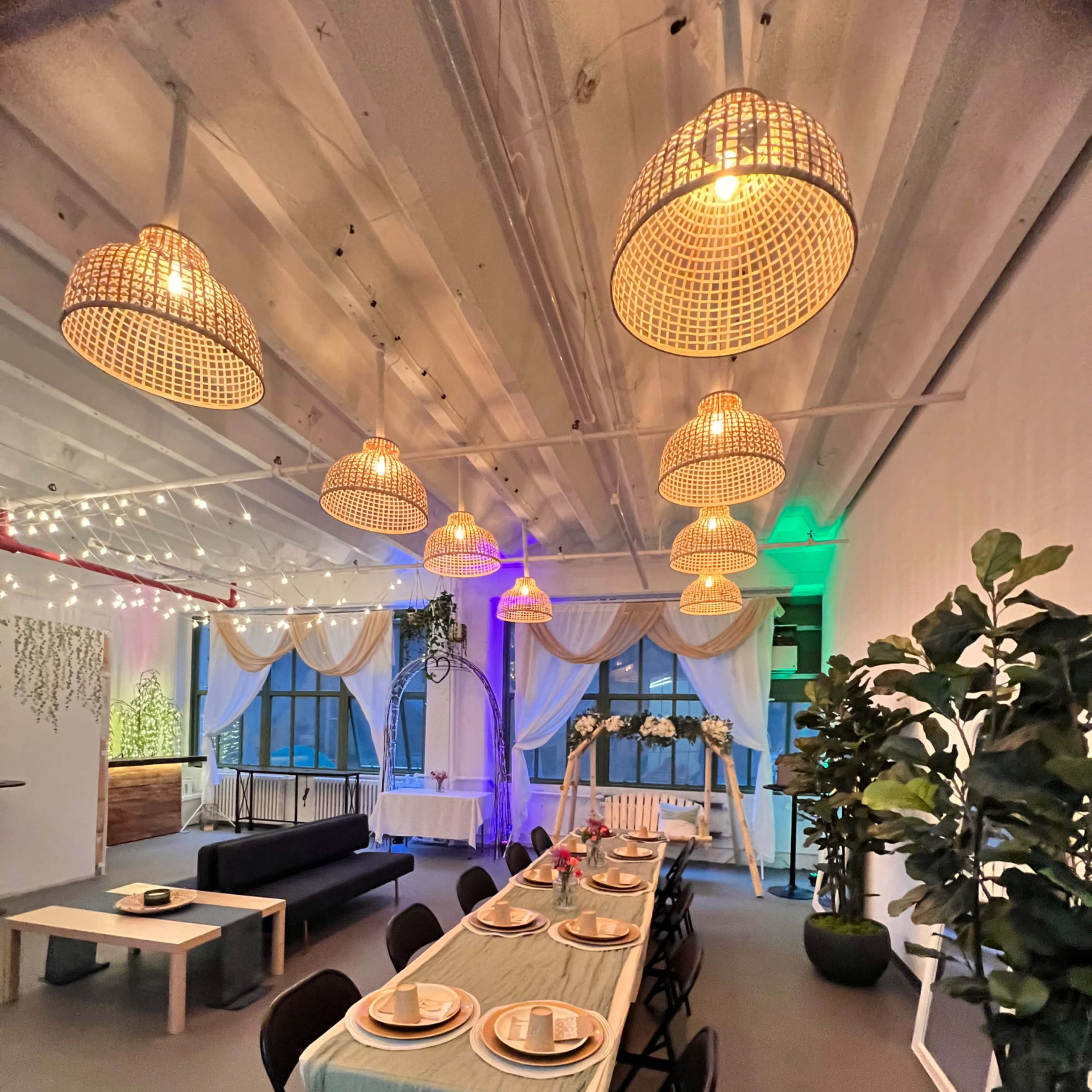 A well-decorated dining area with a long table set for a meal, surrounded by stylish pendant lights and greenery.
