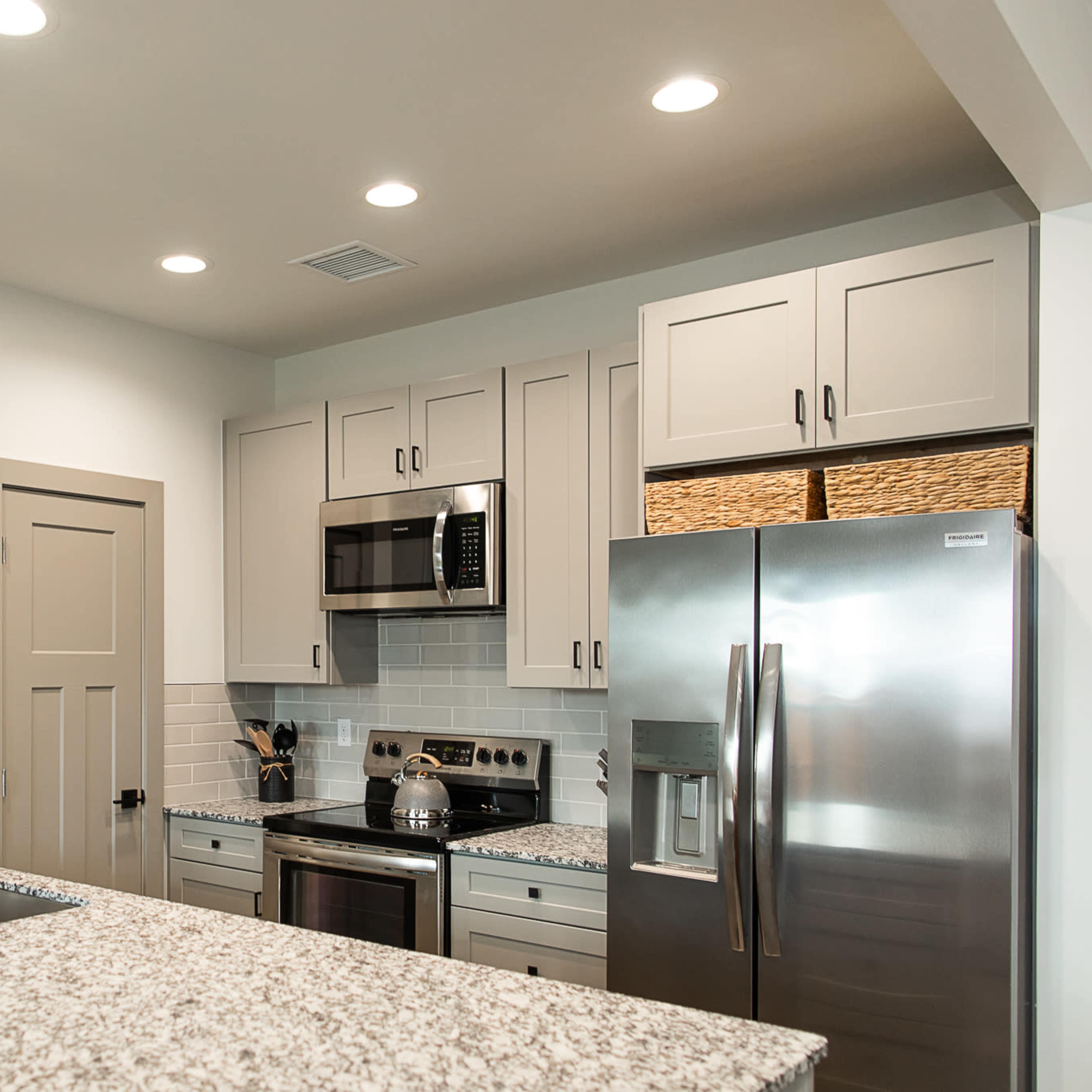 A modern kitchen featuring gray cabinetry, stainless steel appliances, and a large island with a granite countertop.