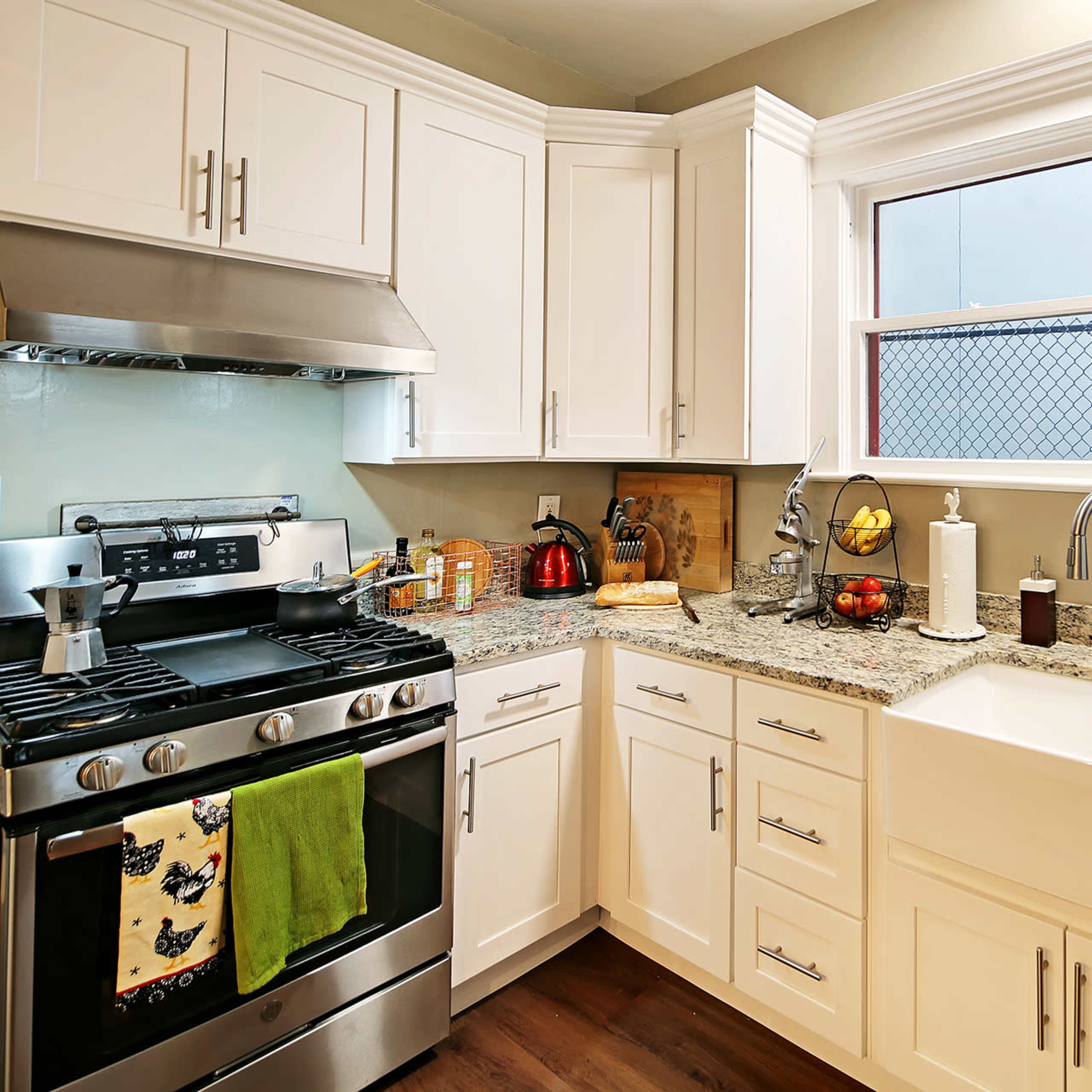 A modern kitchen with white cabinetry, a stainless steel gas stove, and a farmhouse sink.