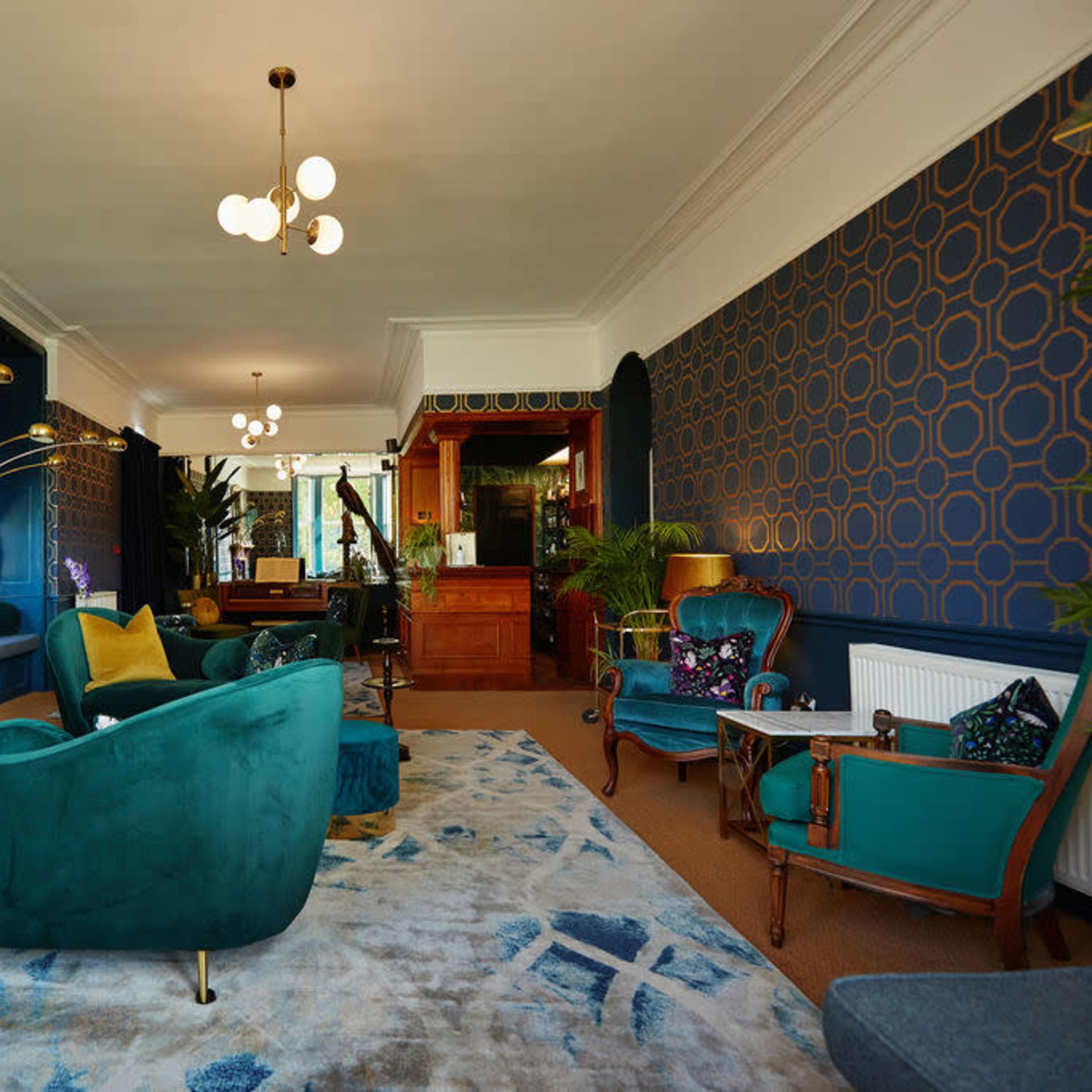 The room features a teal and gold color scheme, with plush seating, a decorative fireplace, and a patterned rug.