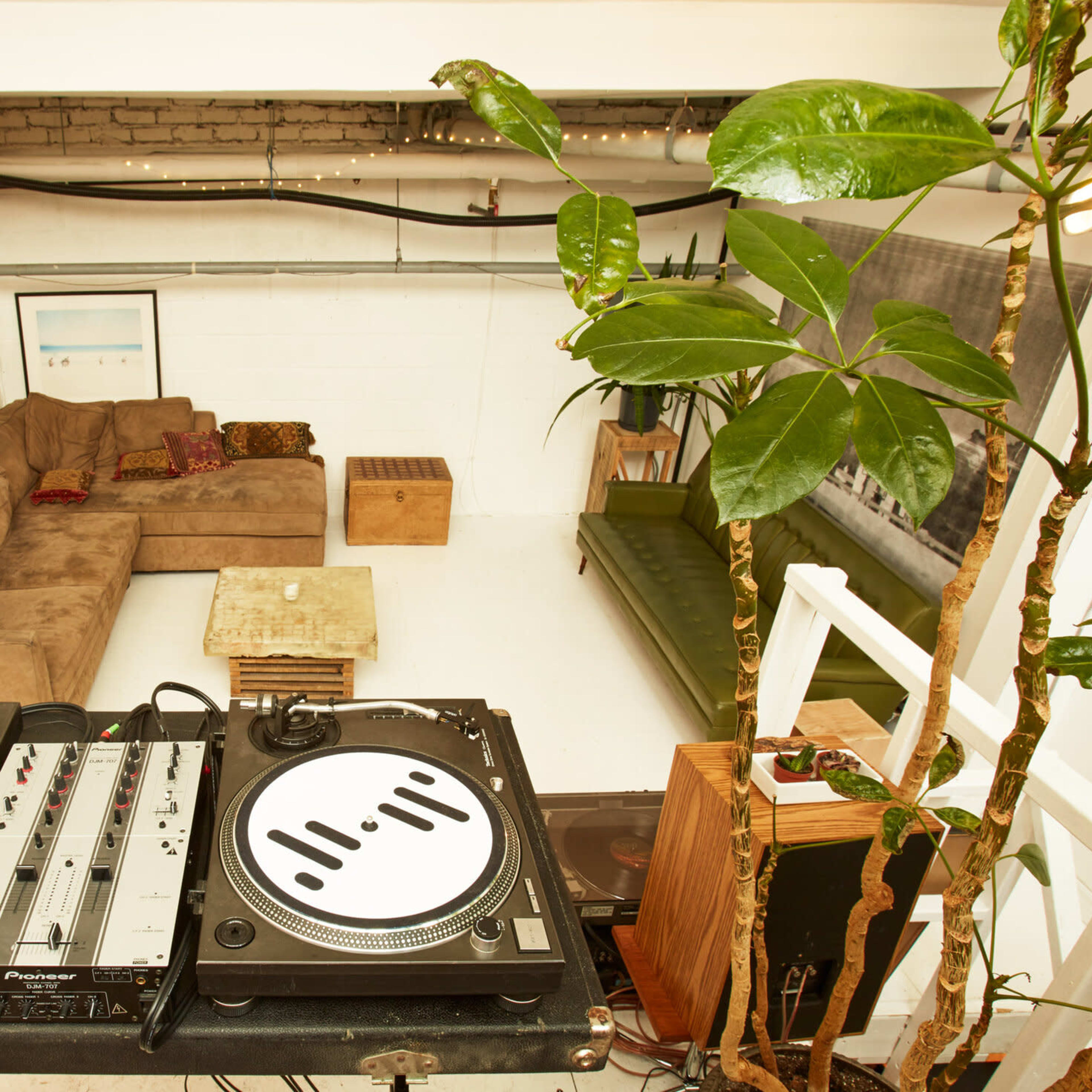 A DJ setup with turntables is positioned in front of a cozy lounge area featuring a brown couch and wooden coffee table.