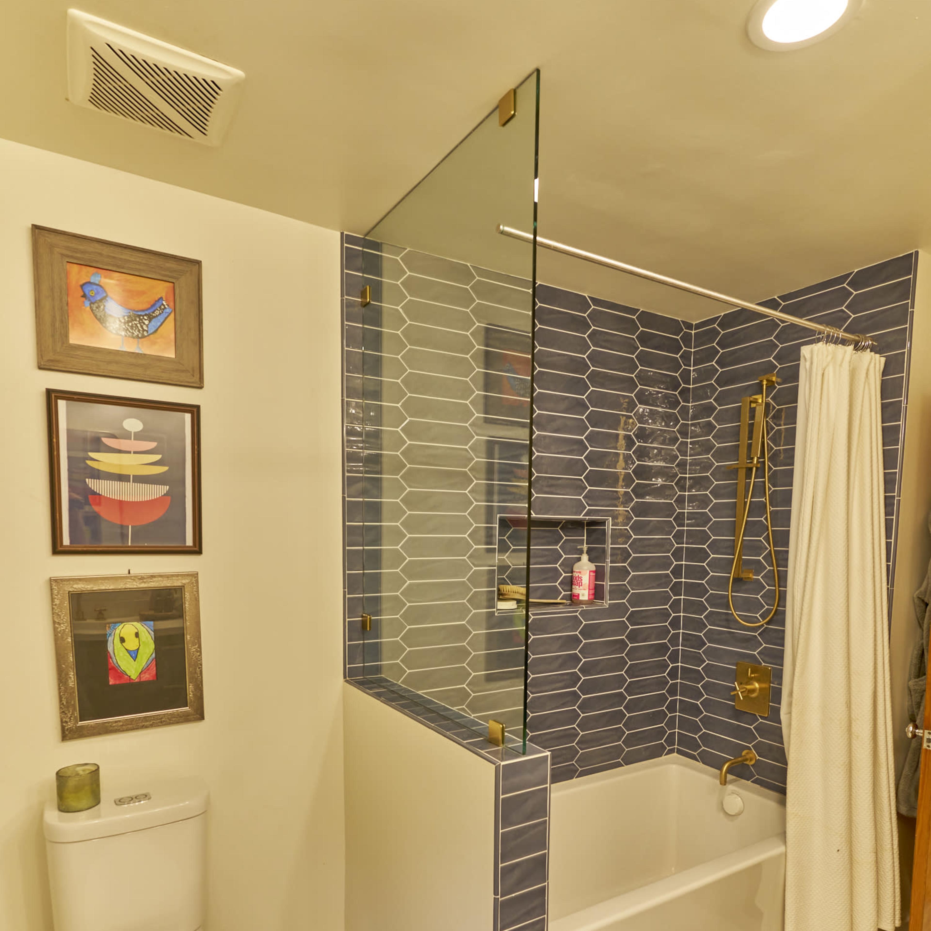 A modern bathroom with a glass shower partition, tiled walls, and a toilet adjacent to a wooden stool.